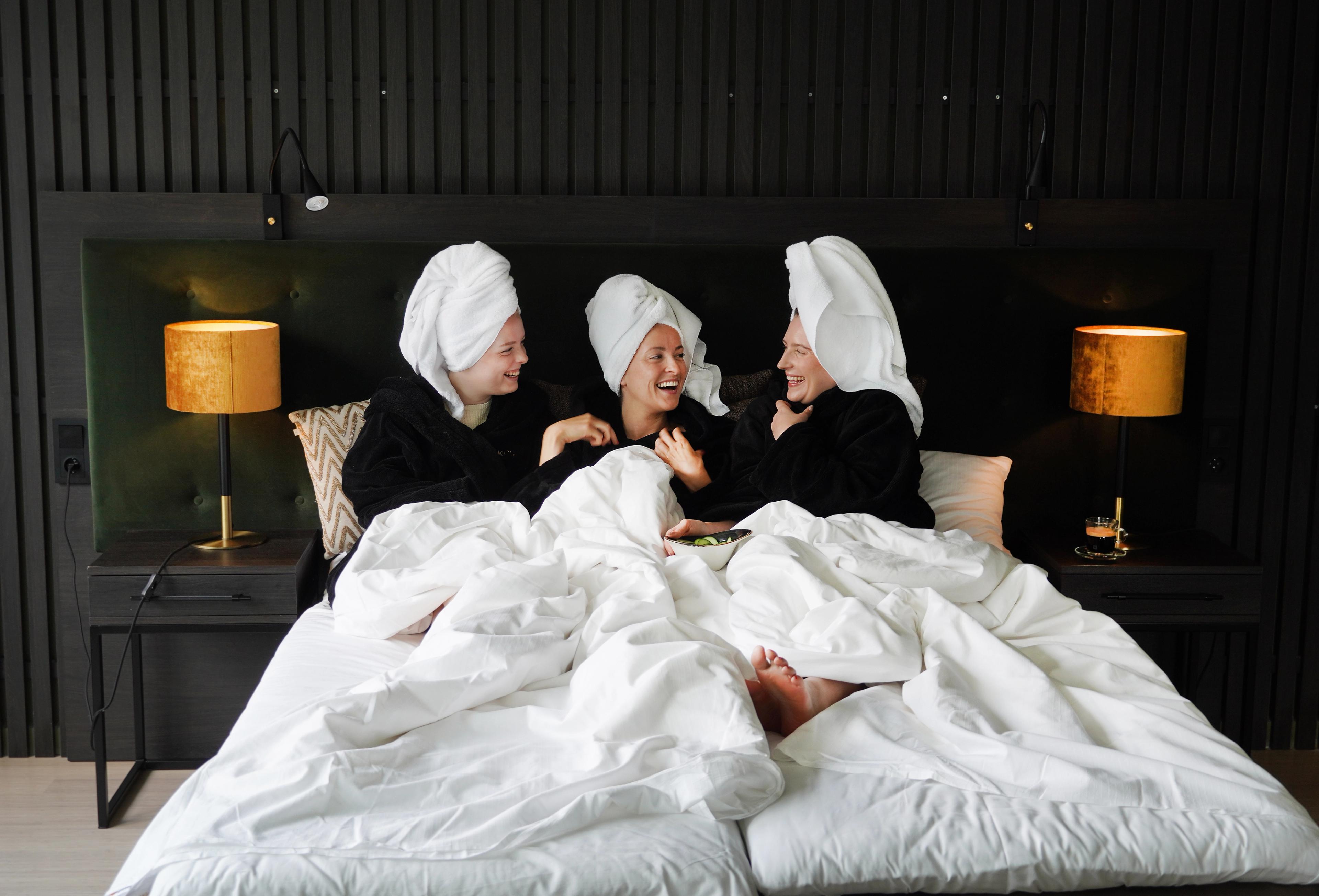 Three girls in a hotel bed smiling.