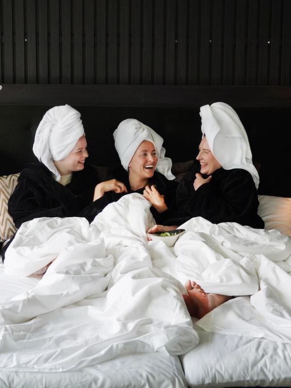 Three girls in a hotel bed smiling.
