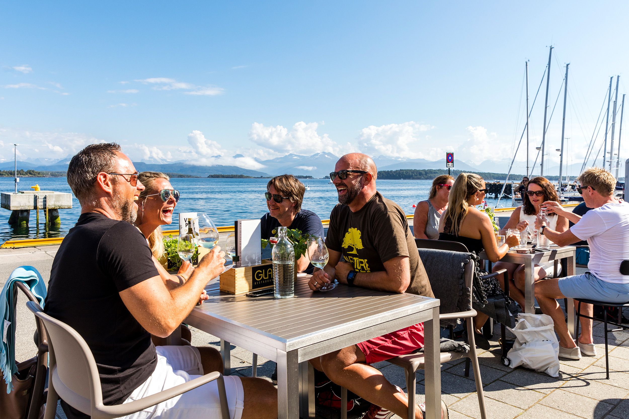 Groups of smiling people sitting in the sun at a restaurant at the waterfront in Molde in Northwest, Fjord Norway.