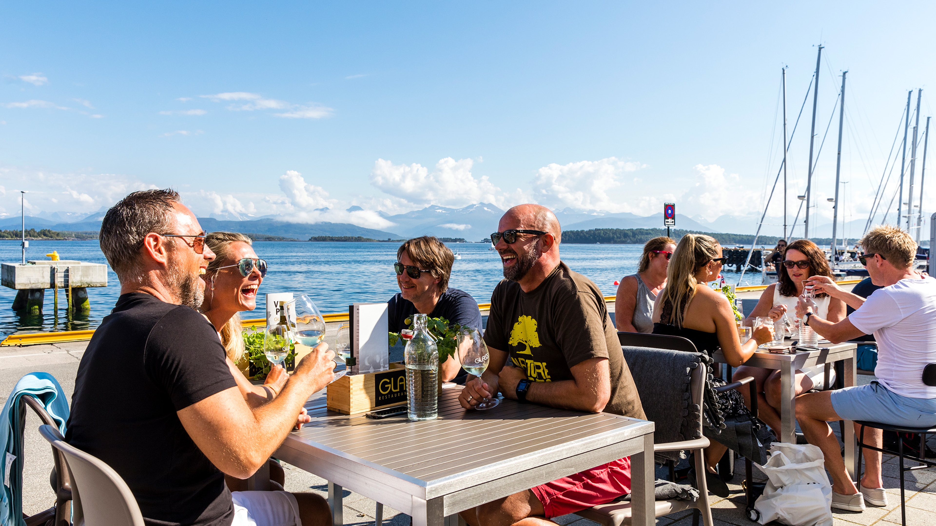 Groups of smiling people sitting in the sun at a restaurant at the waterfront in Molde in Northwest, Fjord Norway.