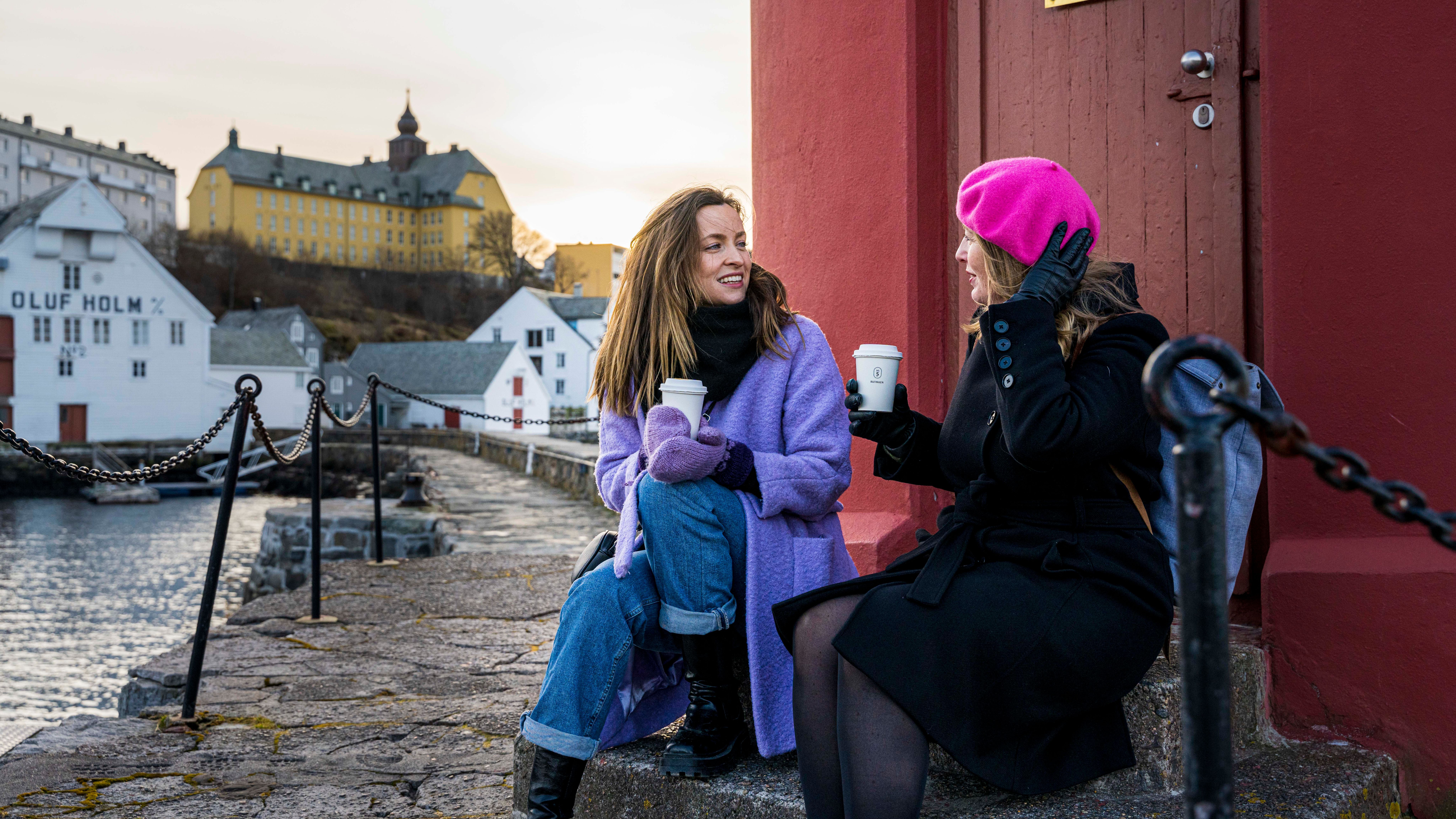 Two women sitting in front of the light house in the harbor of Ålesund