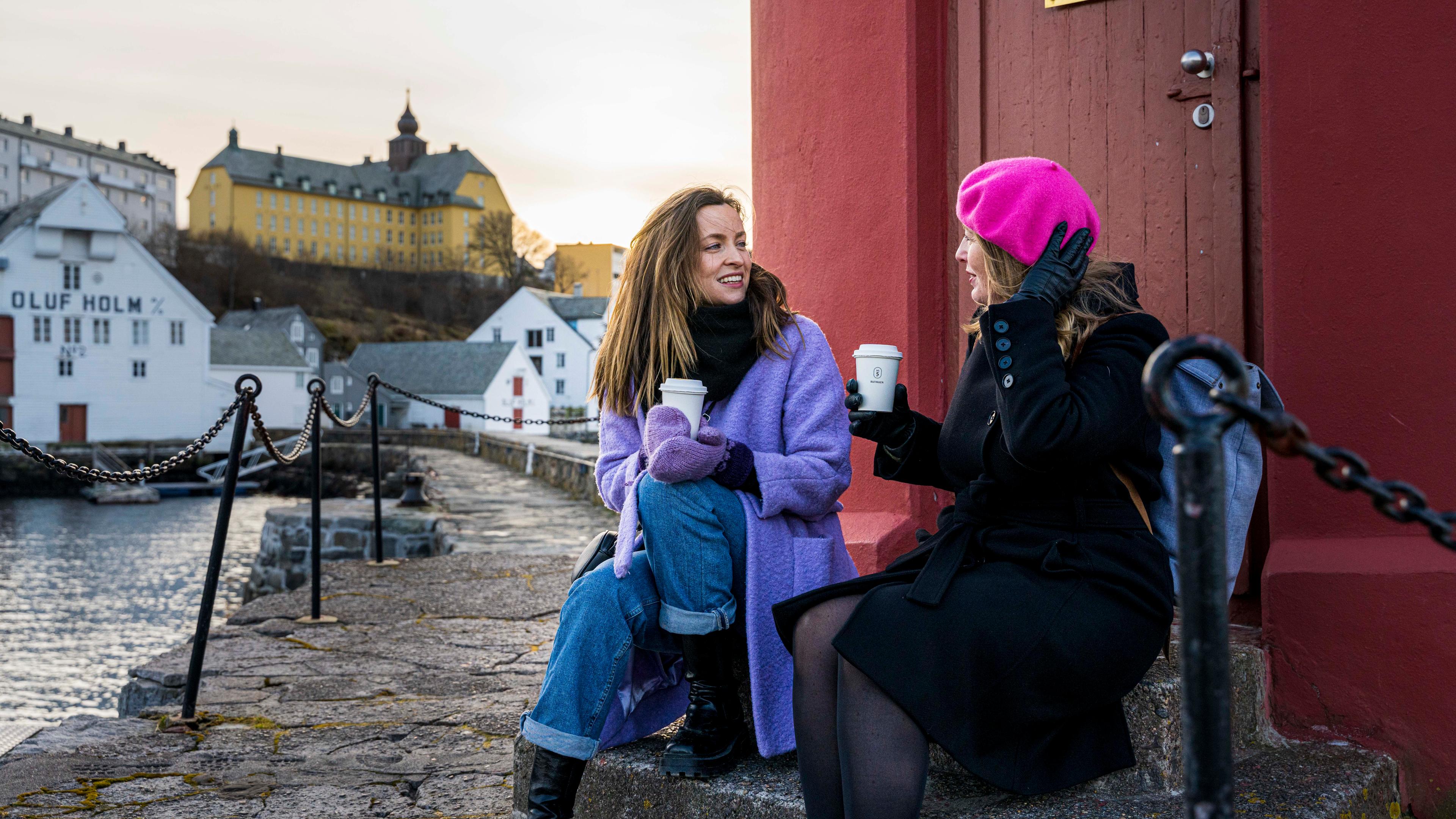 Two women sitting in front of the light house in the harbor of Ålesund