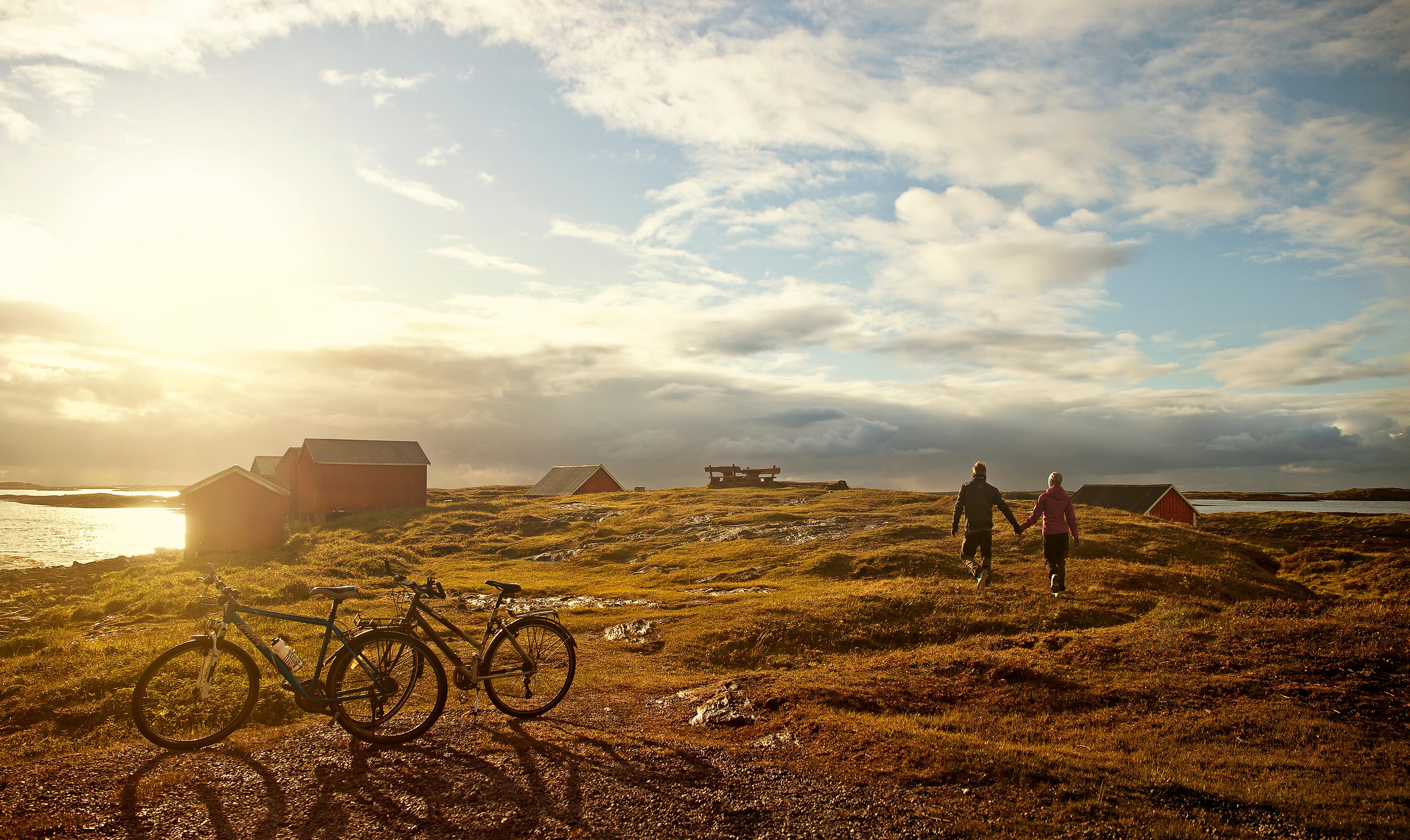 Deux cyclistes ont délaissé leurs vélos pour marcher vers la mer, au soleil couchant, sur l’île de Vega, en Norvège du Nord