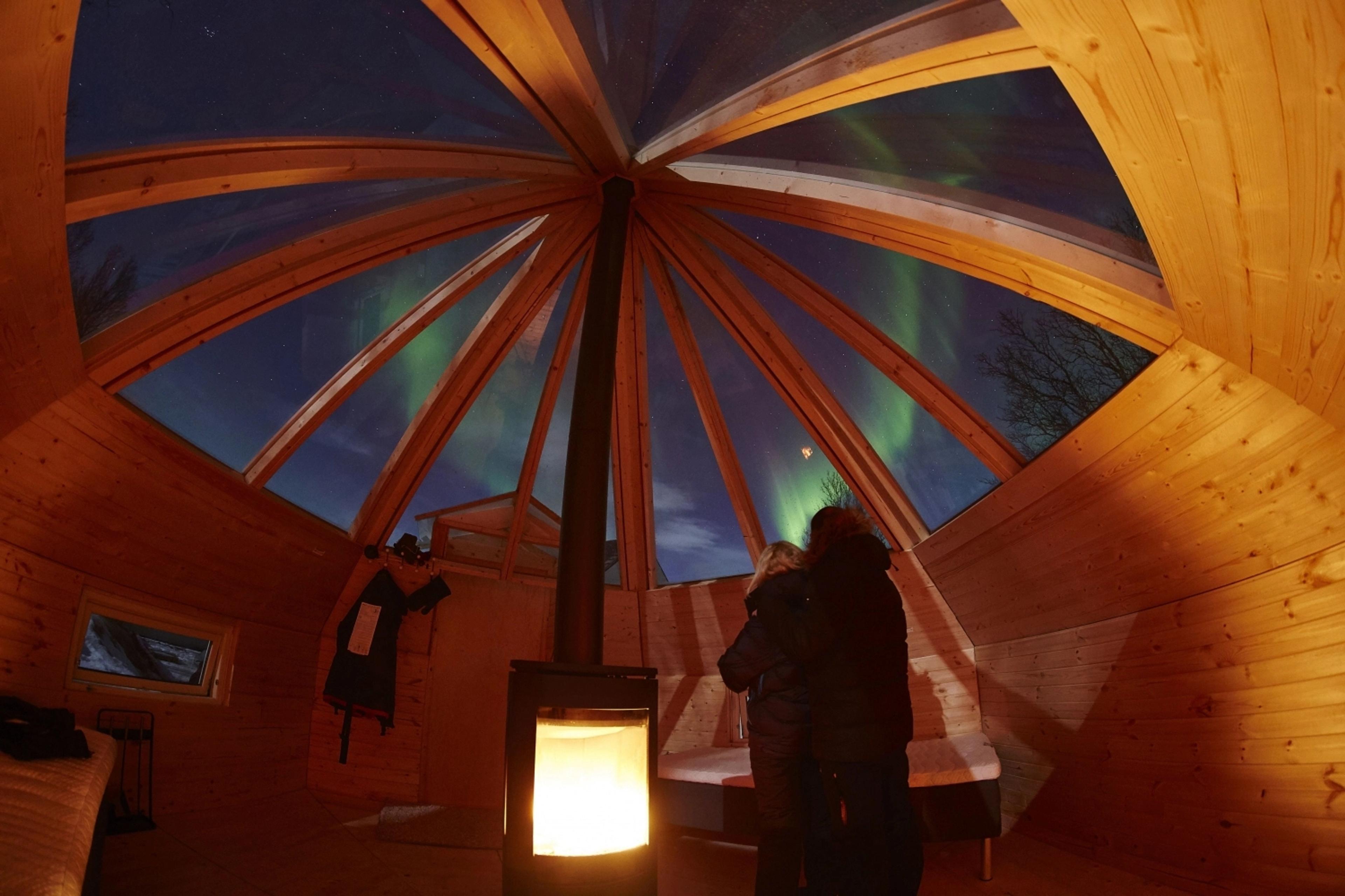 Two people looking at the northern lights through the Crystal Lavvo roof in Tromsø, Northern Norway