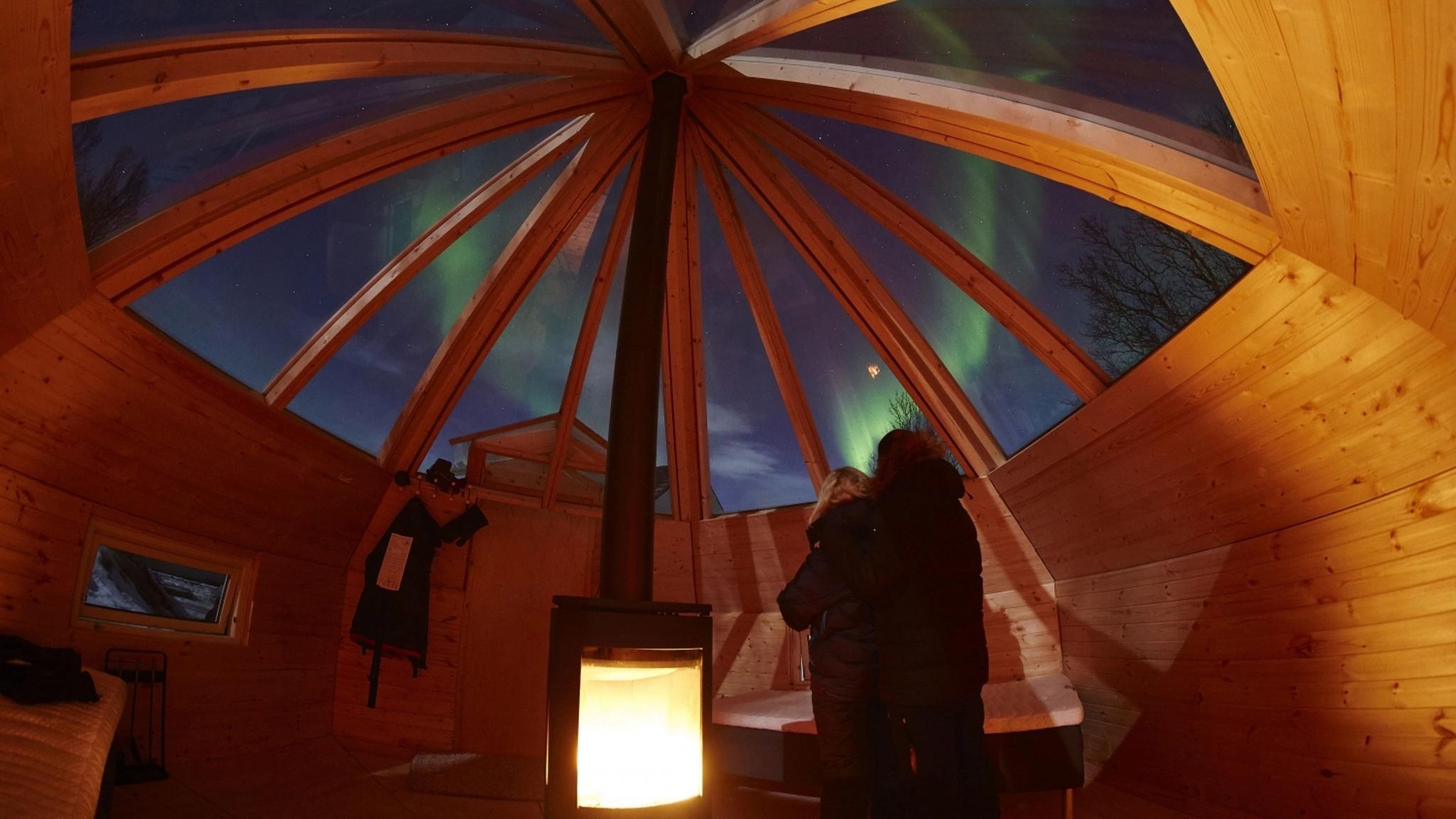 Two people looking at the northern lights through the Crystal Lavvo roof in Tromsø, Northern Norway