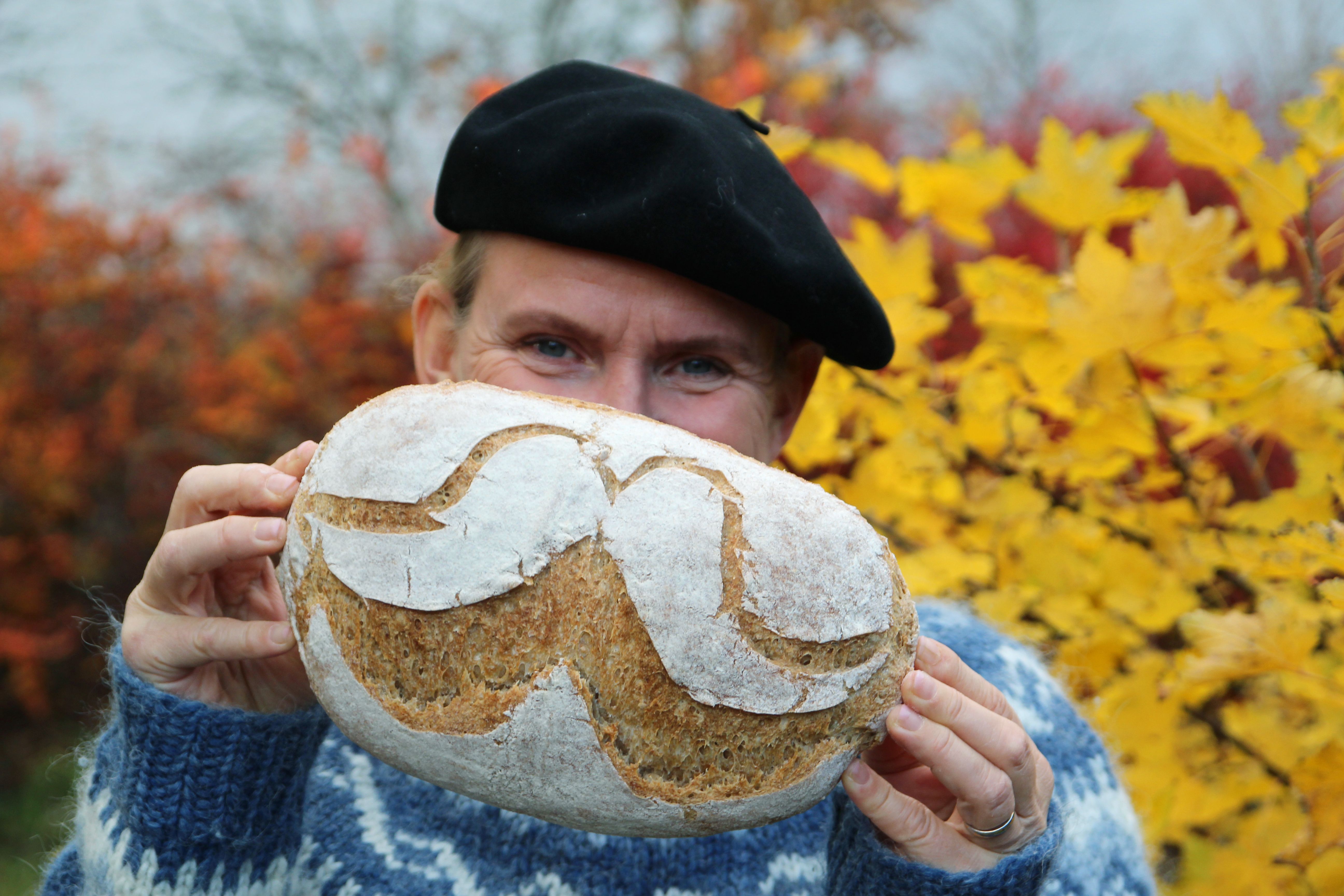 A man is holding up a bread with flour designed as a moustache