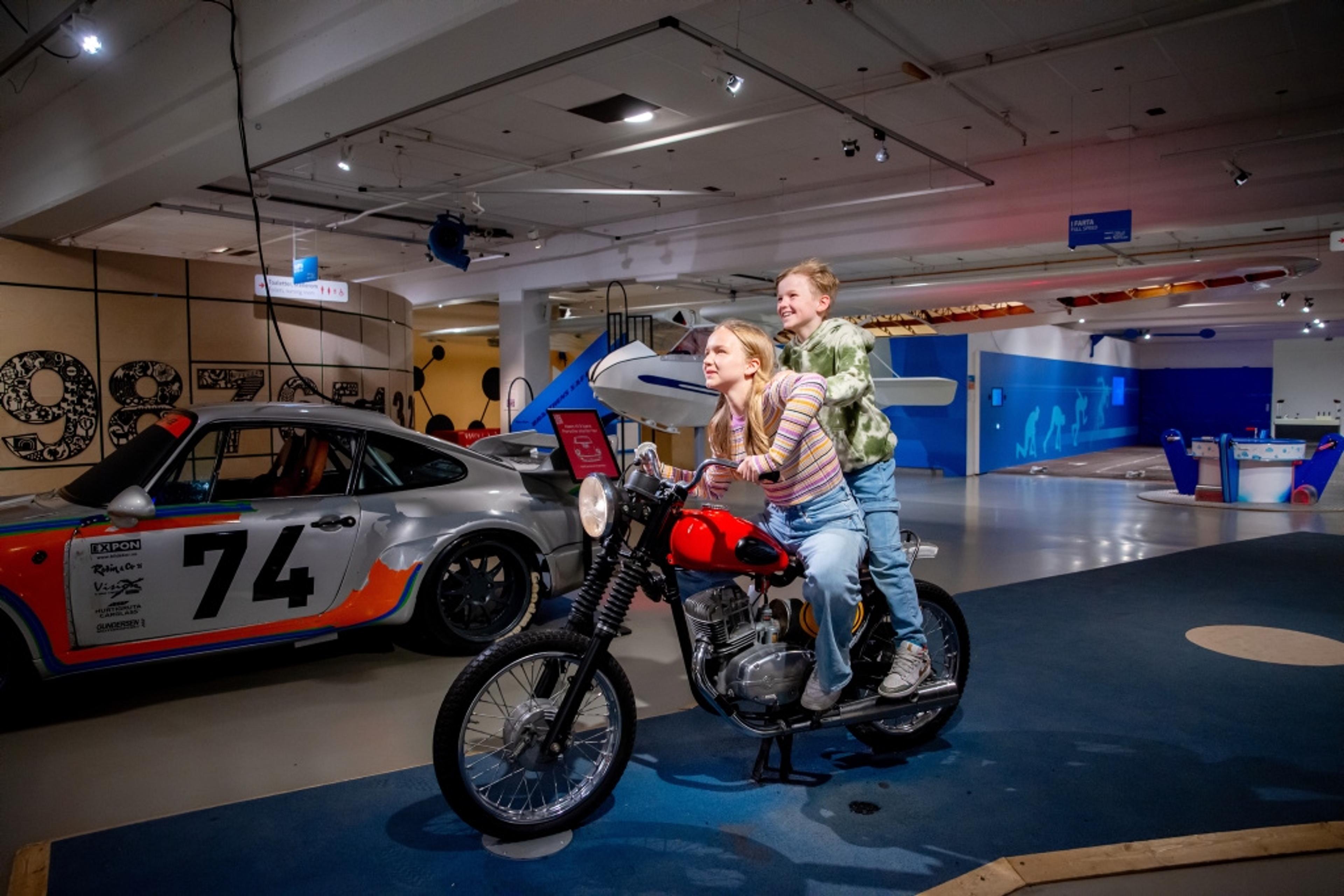 Two kids on a motorcycle in a museum.