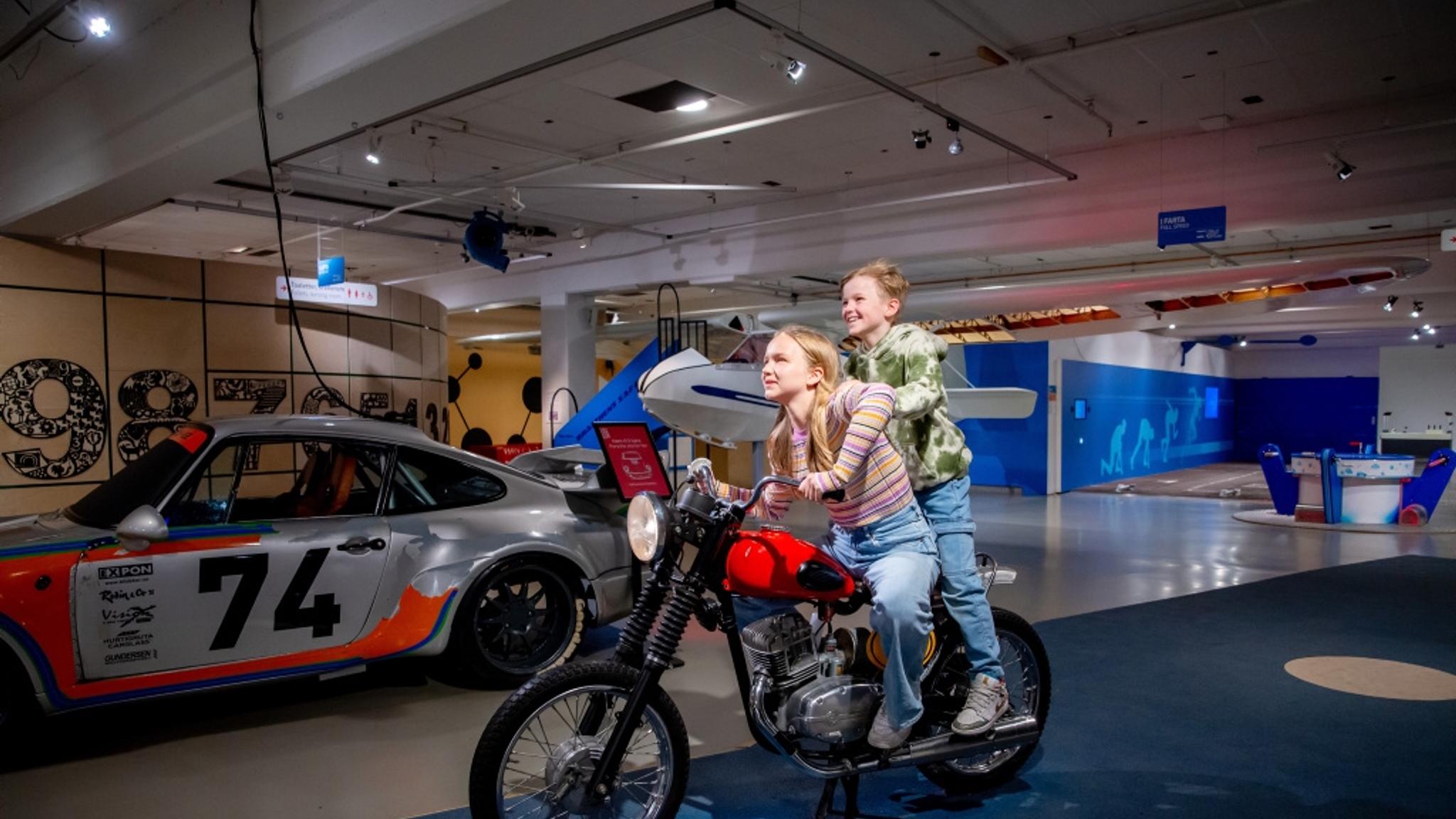Two kids on a motorcycle in a museum.