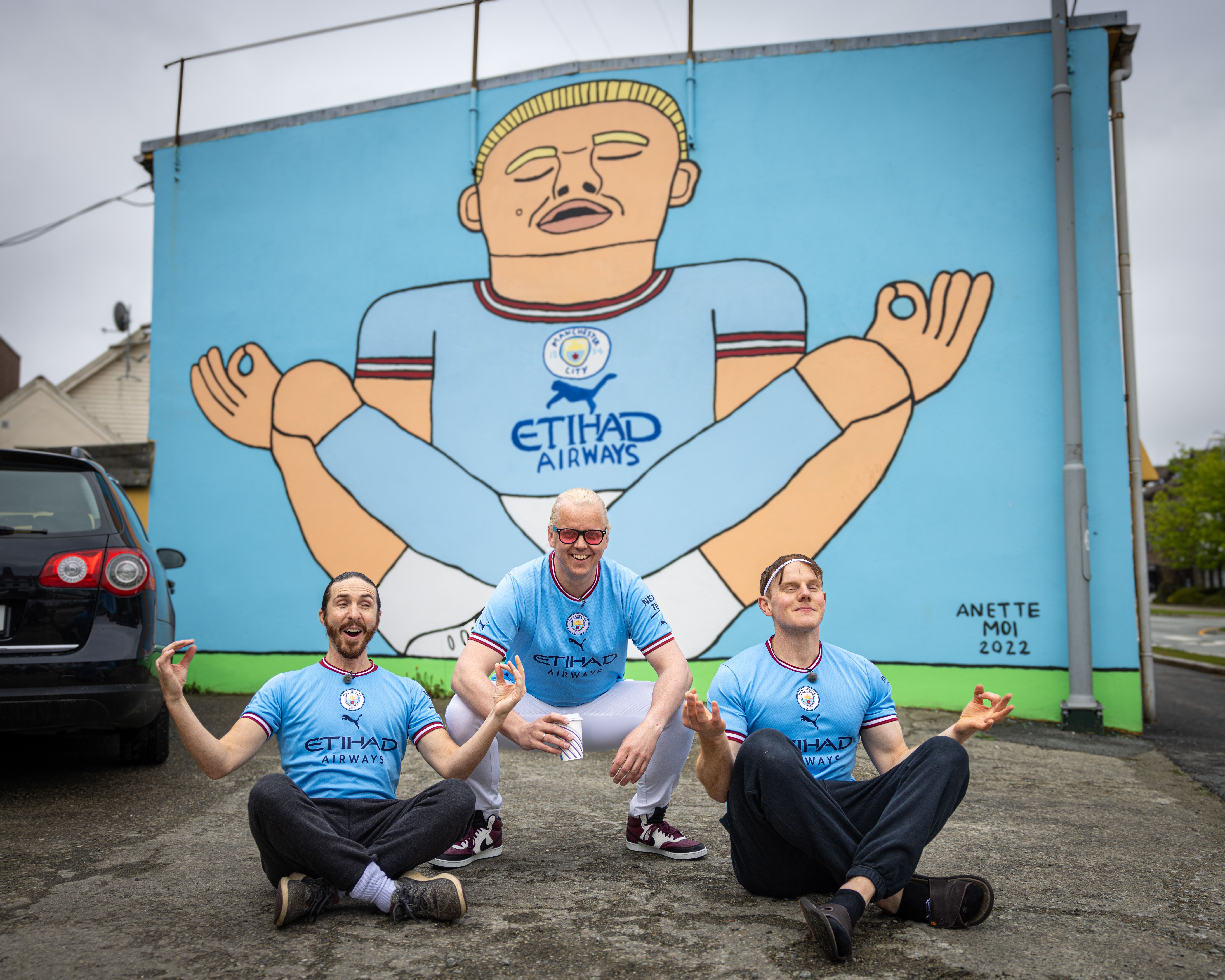 Three men in front of the Erling Braut Haaland street art by Anette Moi in Bryne, Fjord Norway