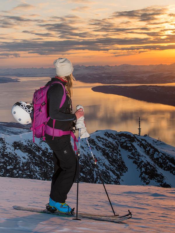 Two women with skis enjoying the view of mountains and fjord from the top of a mountain in Narvik, Northern Norway