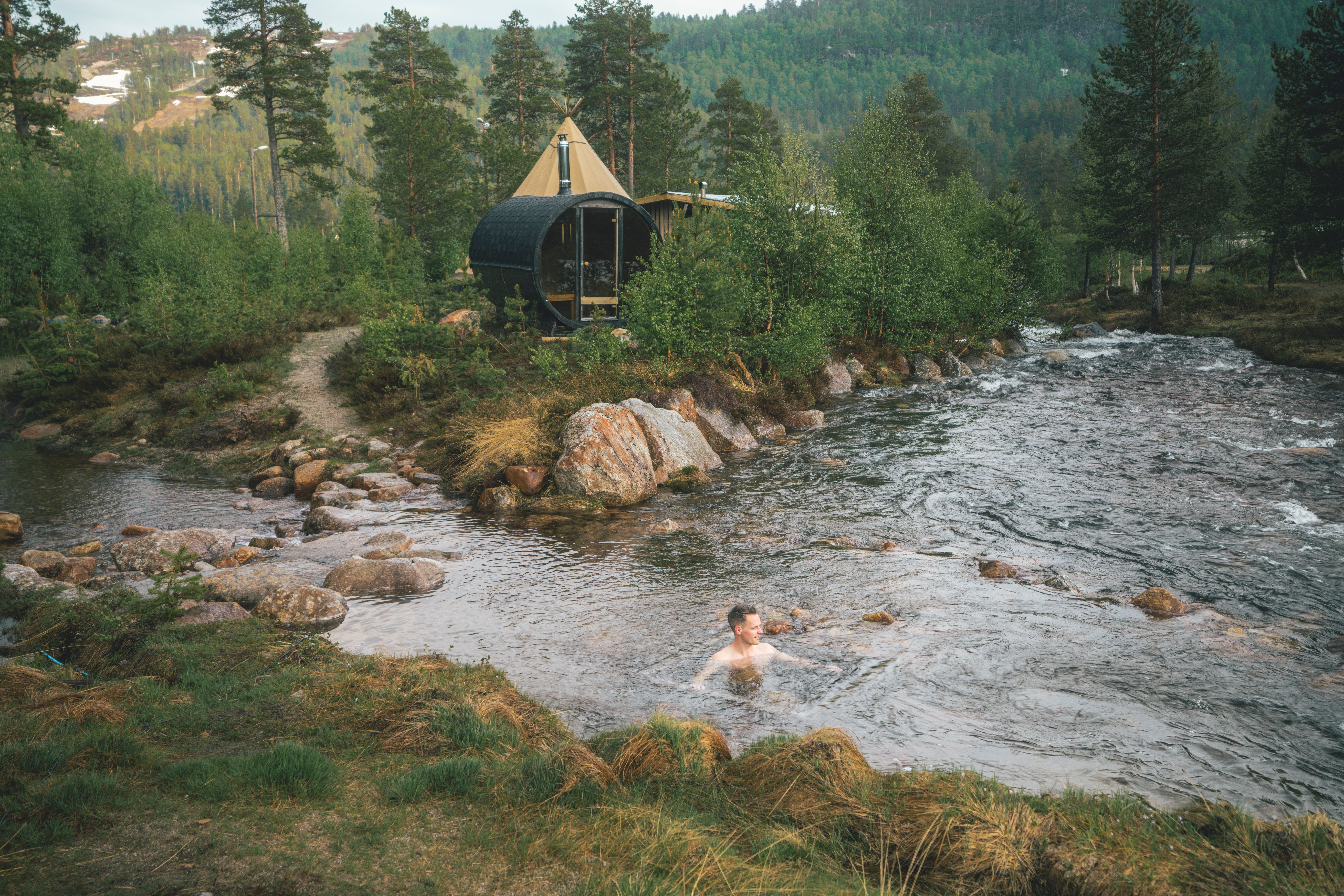 A man taking a cold plunge in the river at Brokkestøylen glamping