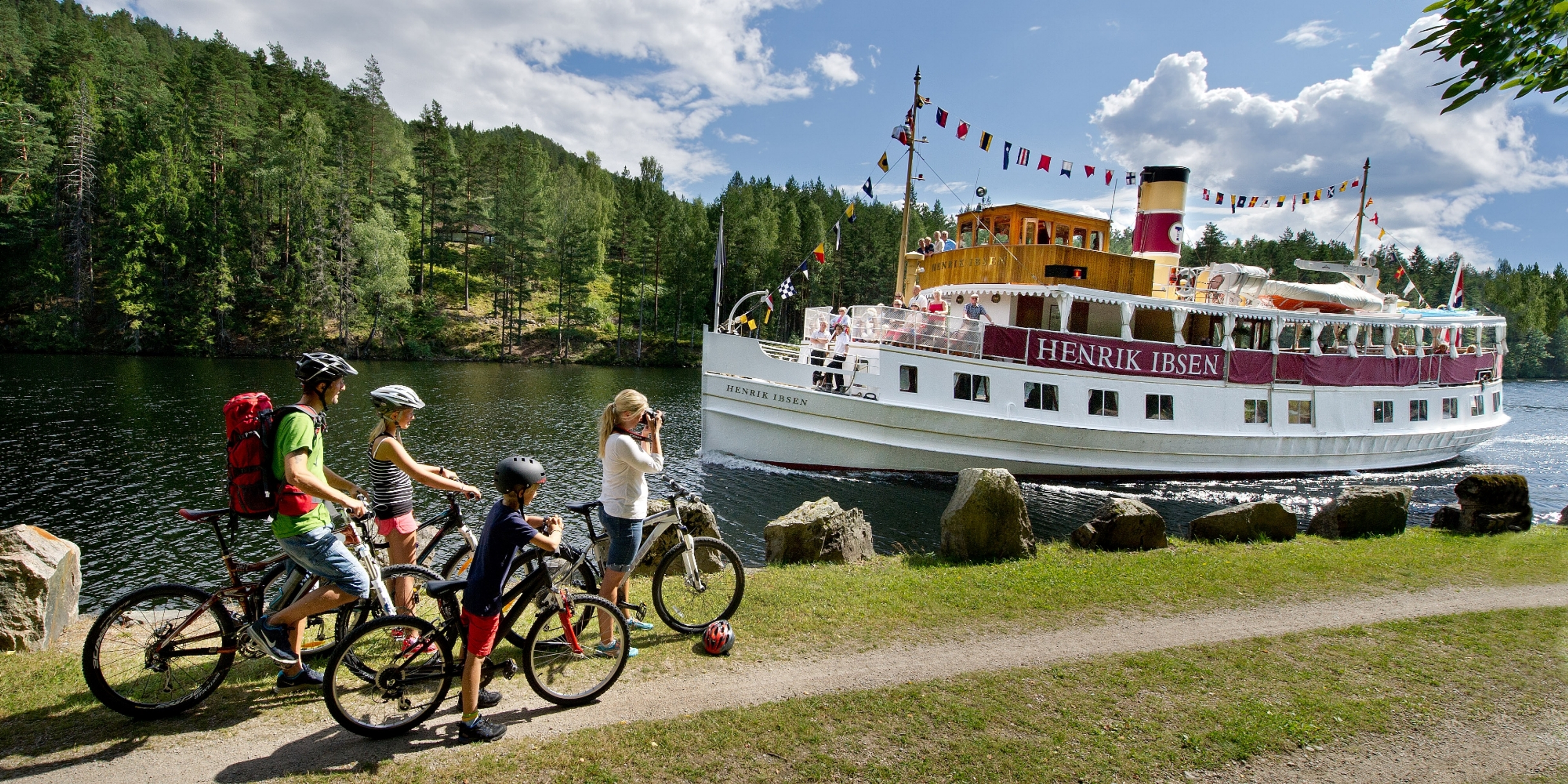 A family cycling past M/S Henrik Ibsen on the Telemark Canal in Eastern Norway