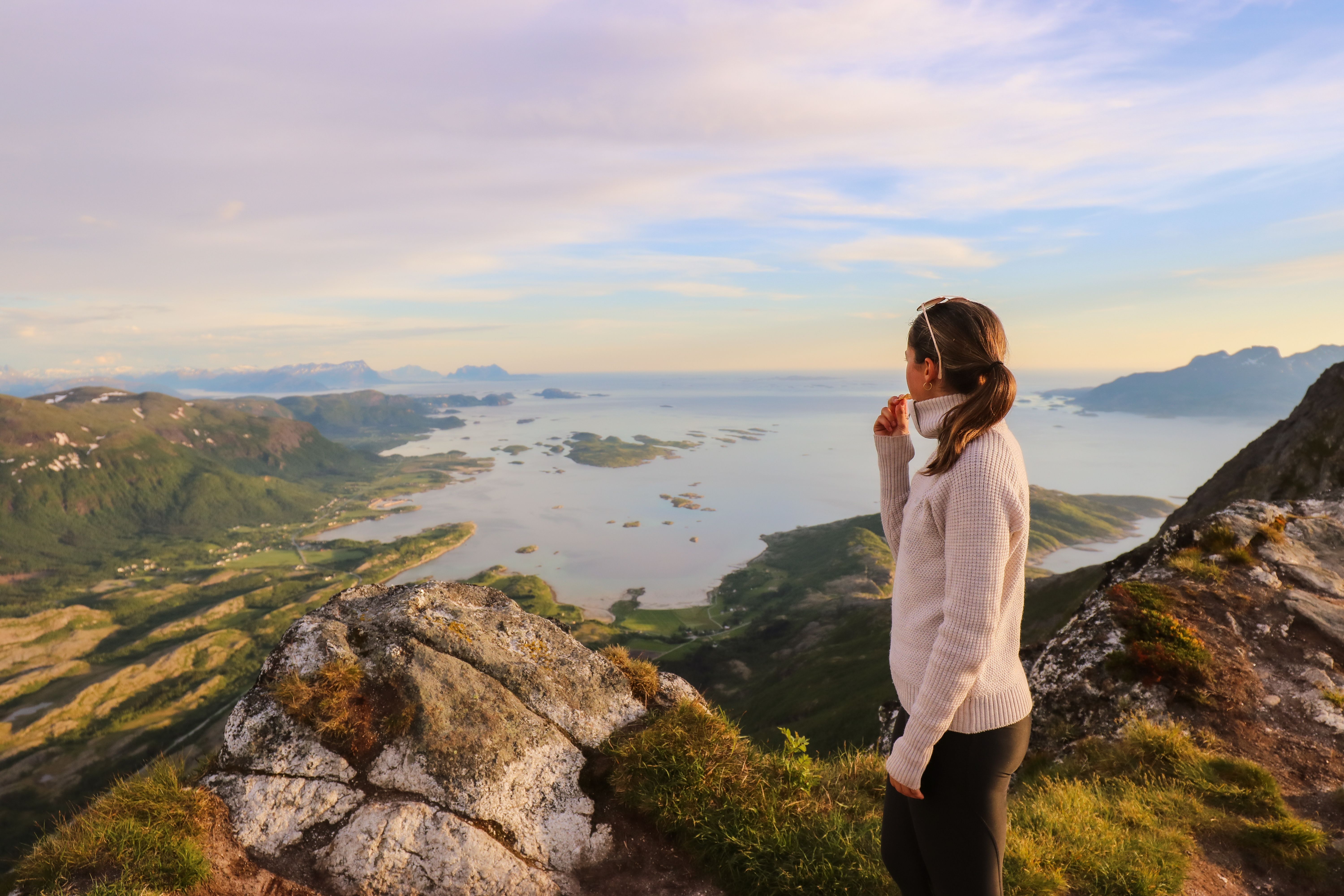A woman standing on Litltind mountain in Bodø in midnight sun.