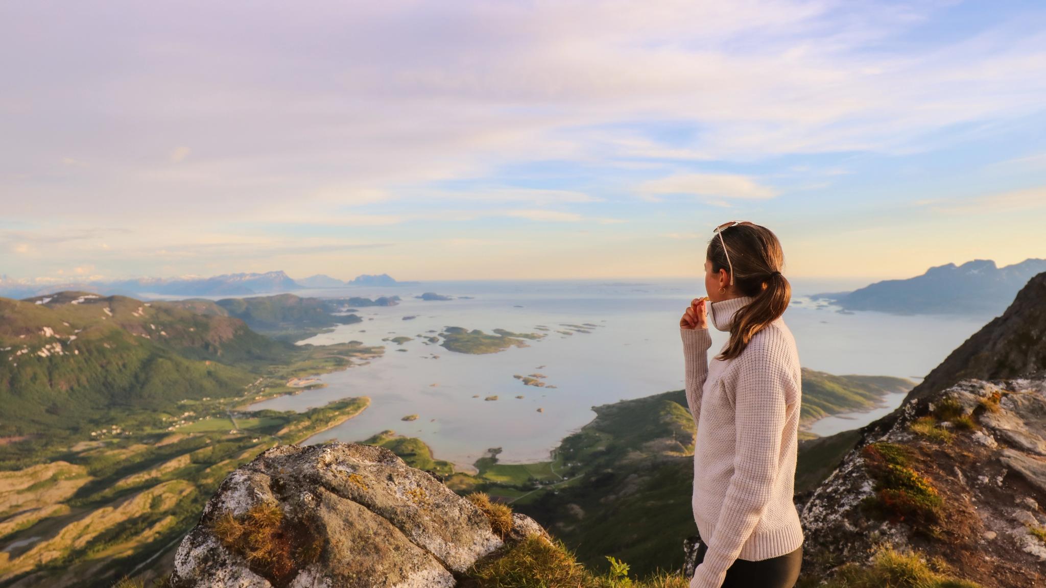 A woman standing on Litltind mountain in Bodø in midnight sun.