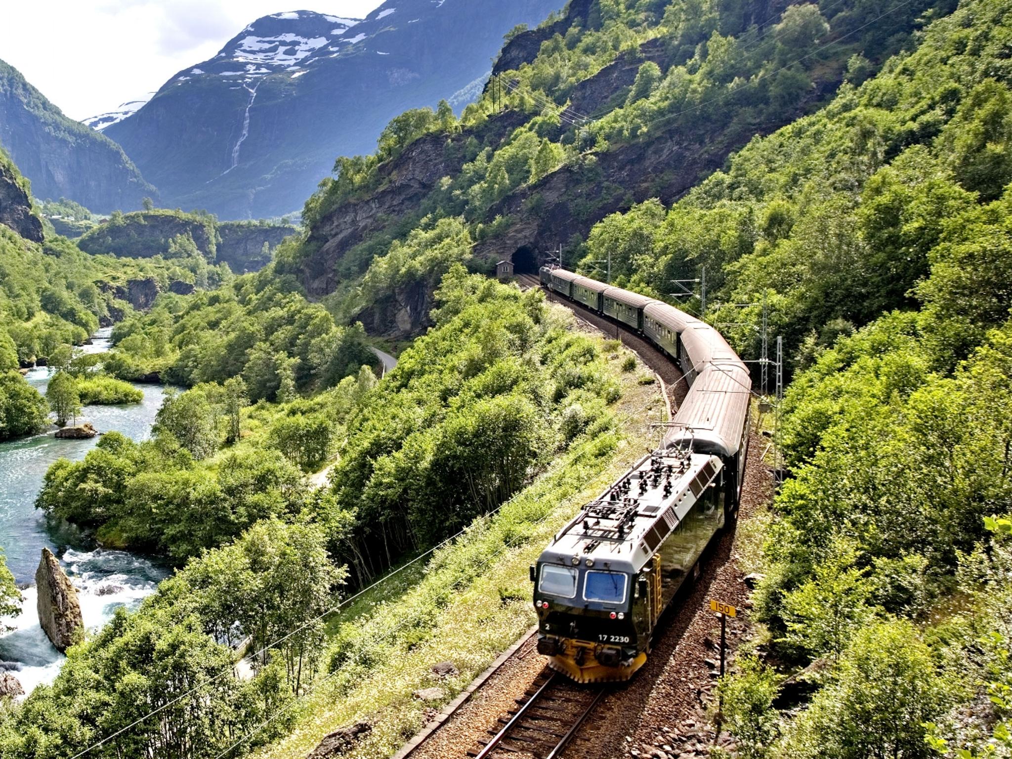 Et tog kjører på Flåmsbana gjennom en grønn og frodig dal