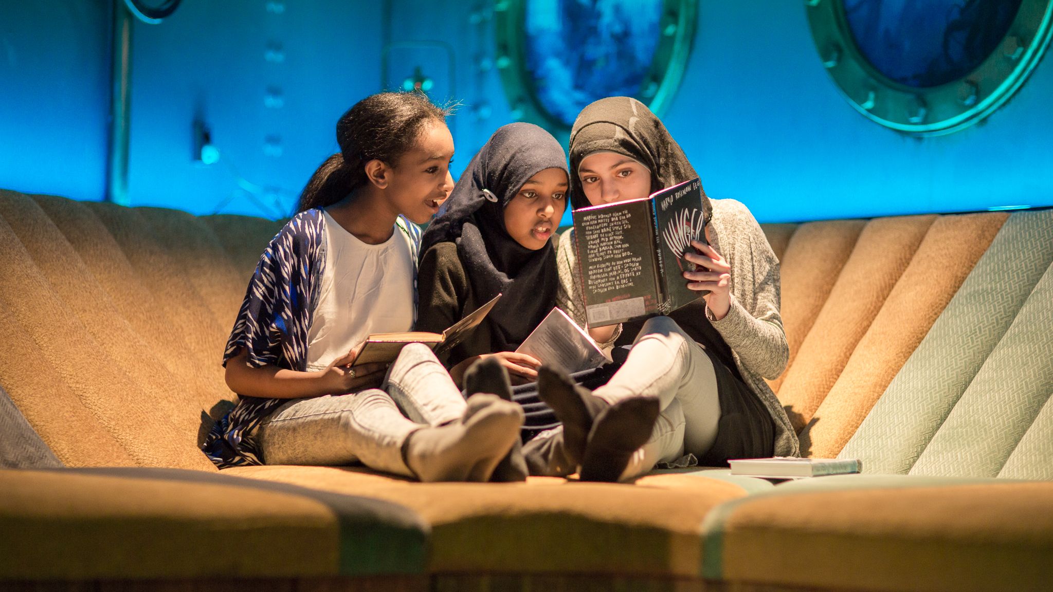 Three girls reading a book in the Biblo Tøyen library, Oslo, Eastern Norway