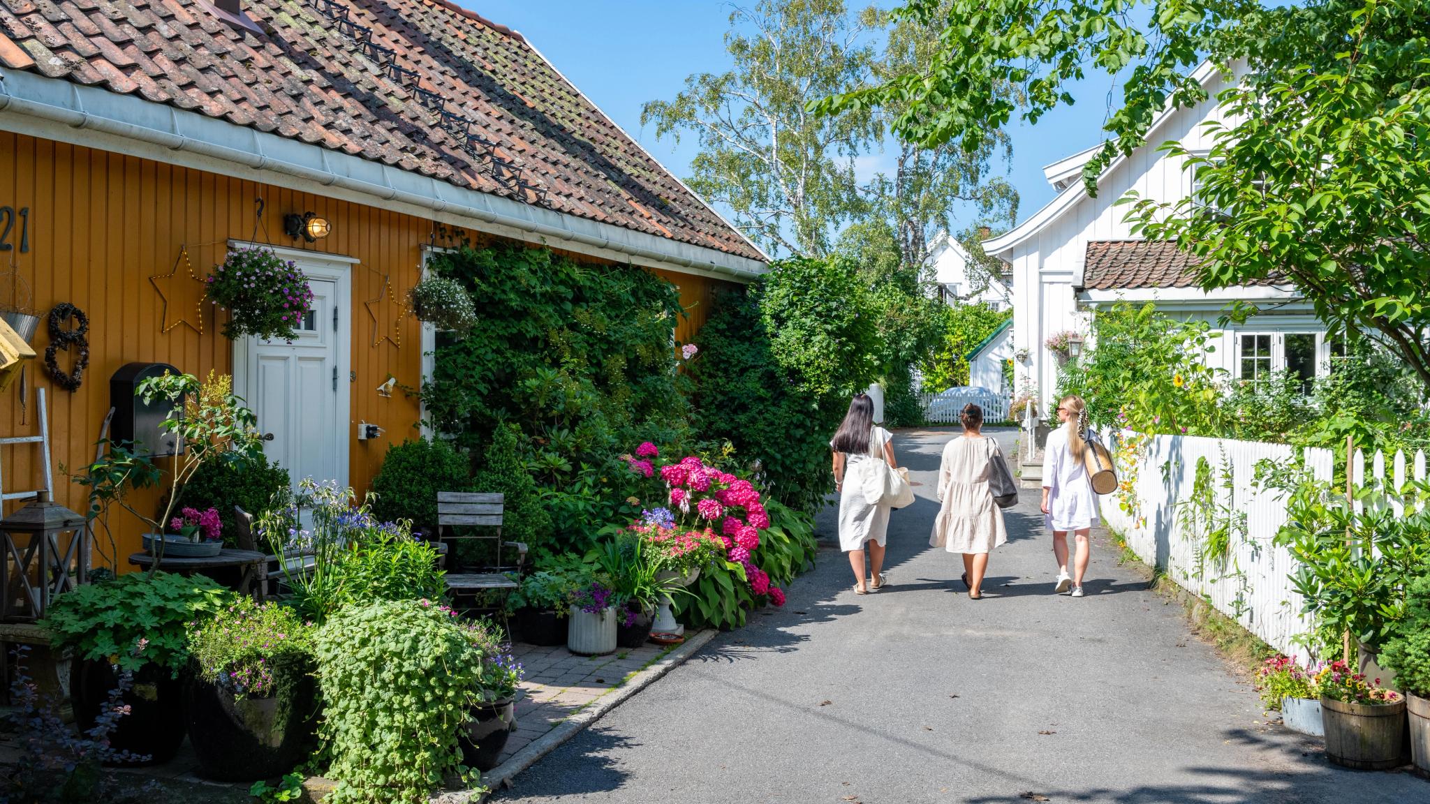 Three women walking past wooden houses in Drøbak