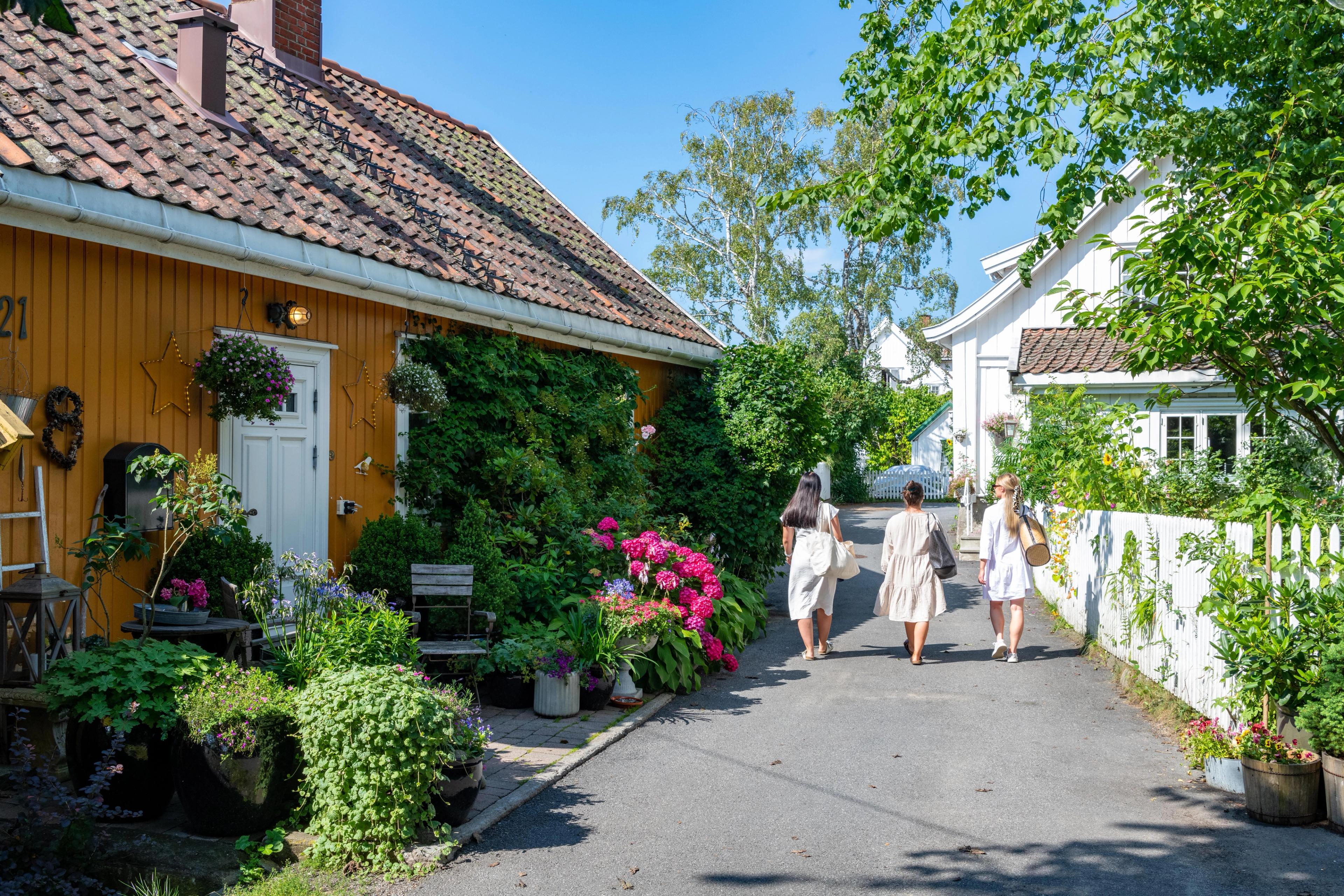 Three women walking past wooden houses in Drøbak