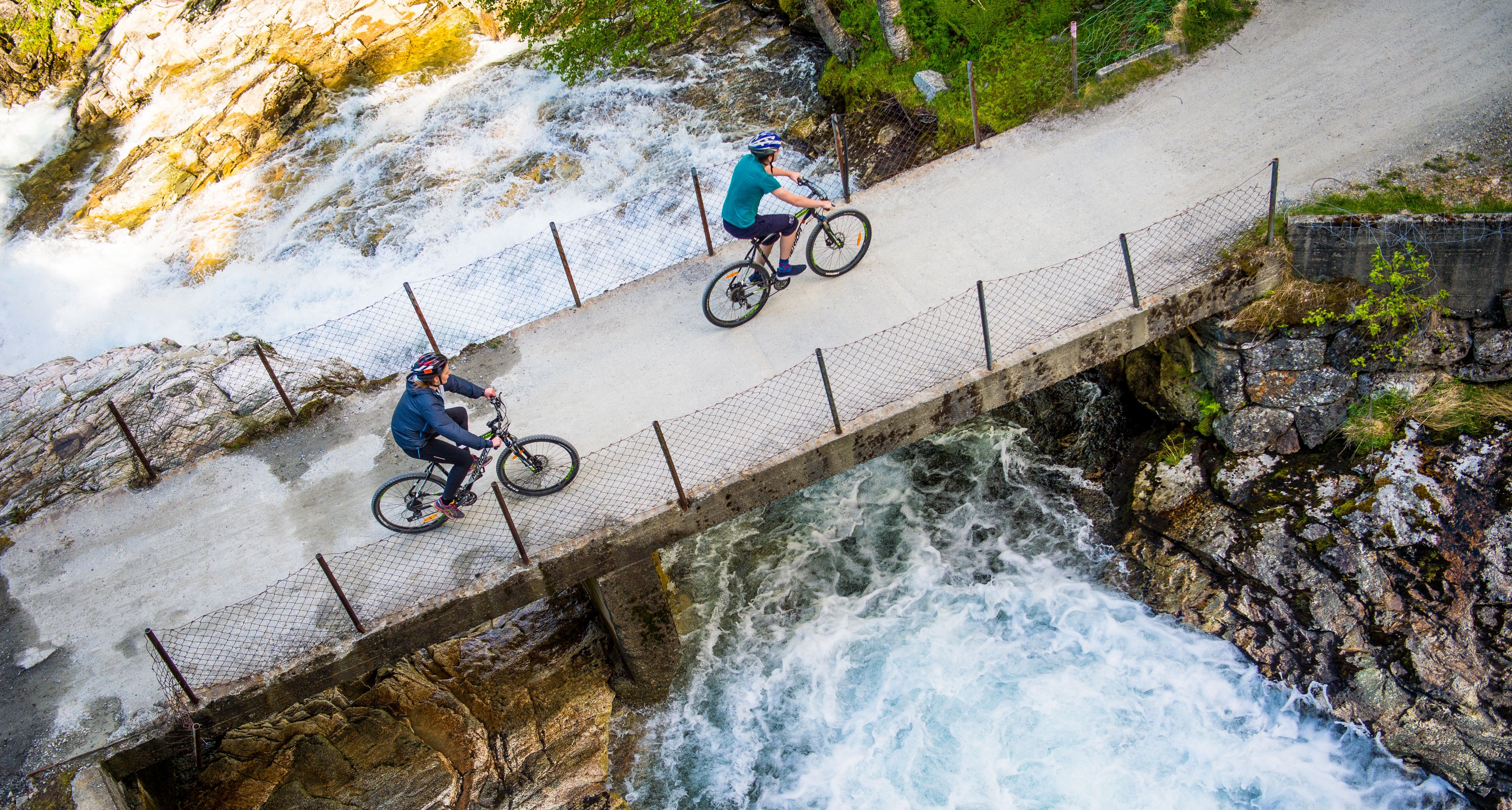 Två cyklister som cyklar över en bro över en älv på Rallarvegen, Fjord-Norge