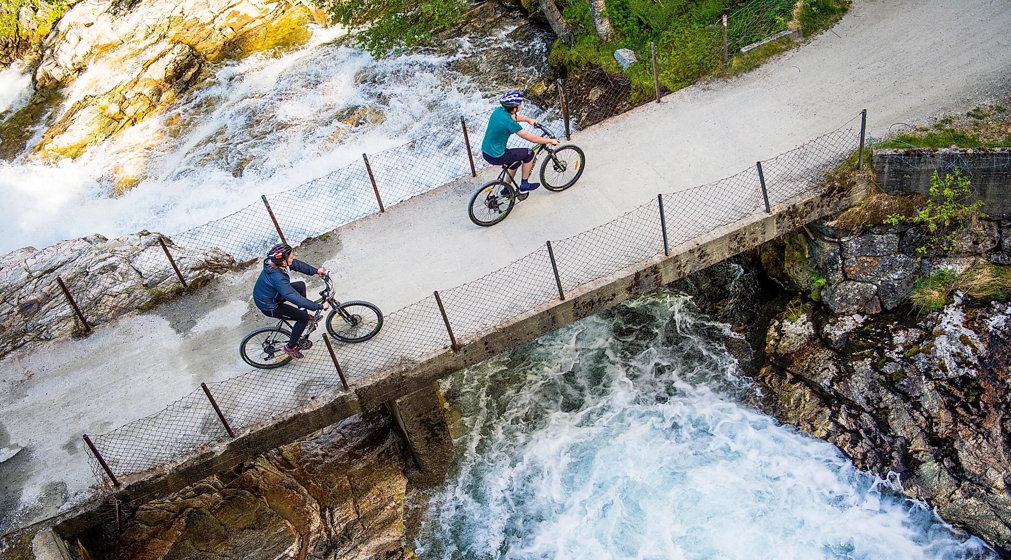 Two cyclists crossing a bridge on the river on the Rallarvegen, Fjord Norway