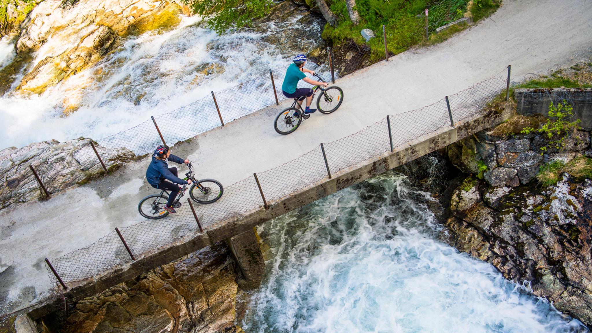 Två cyklister som cyklar över en bro över en älv på Rallarvegen, Fjord-Norge