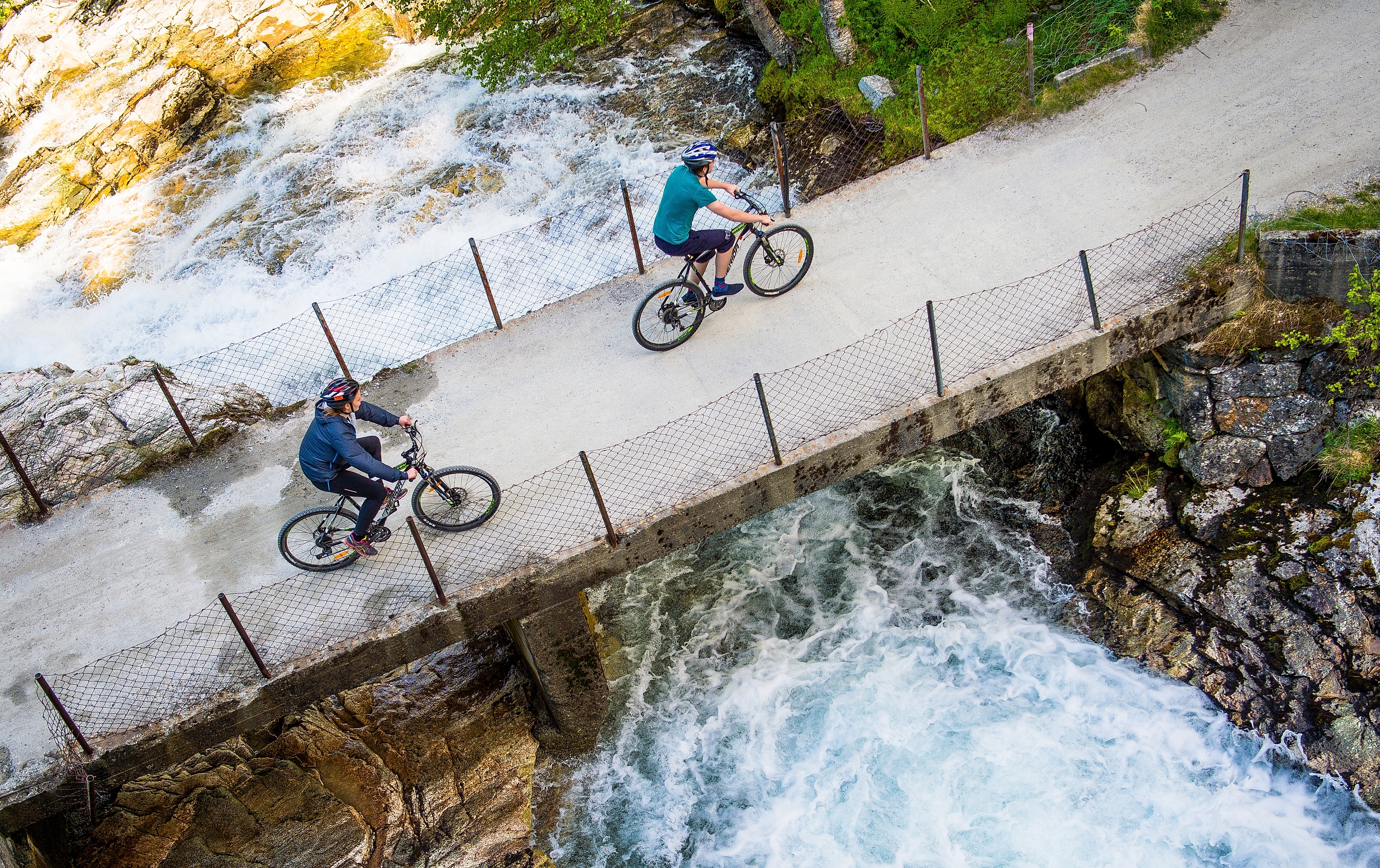 Two cyclists crossing a bridge on the river on the Rallarvegen, Fjord Norway