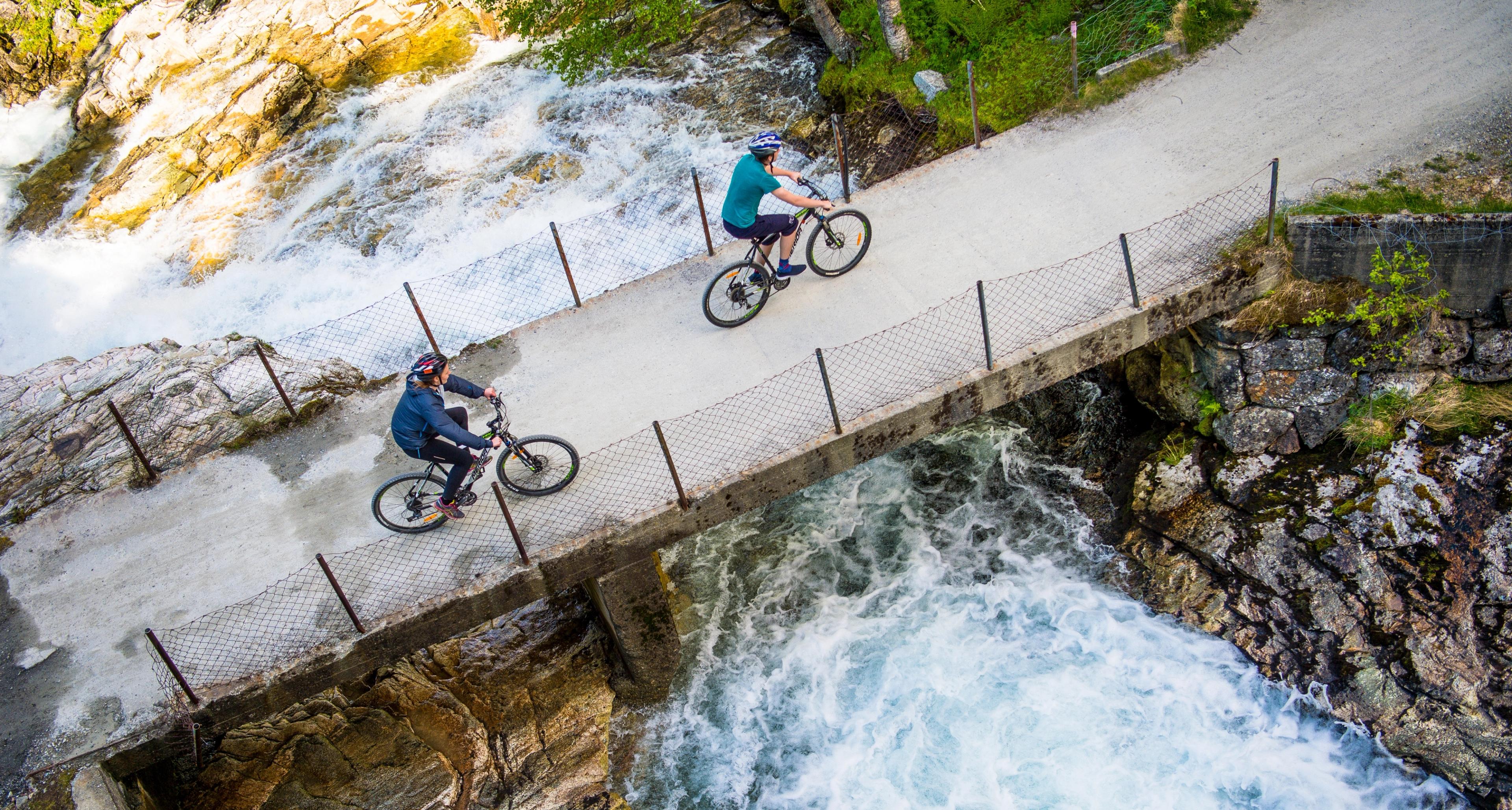 Two cyclists crossing a bridge on the river on the Rallarvegen, Fjord Norway