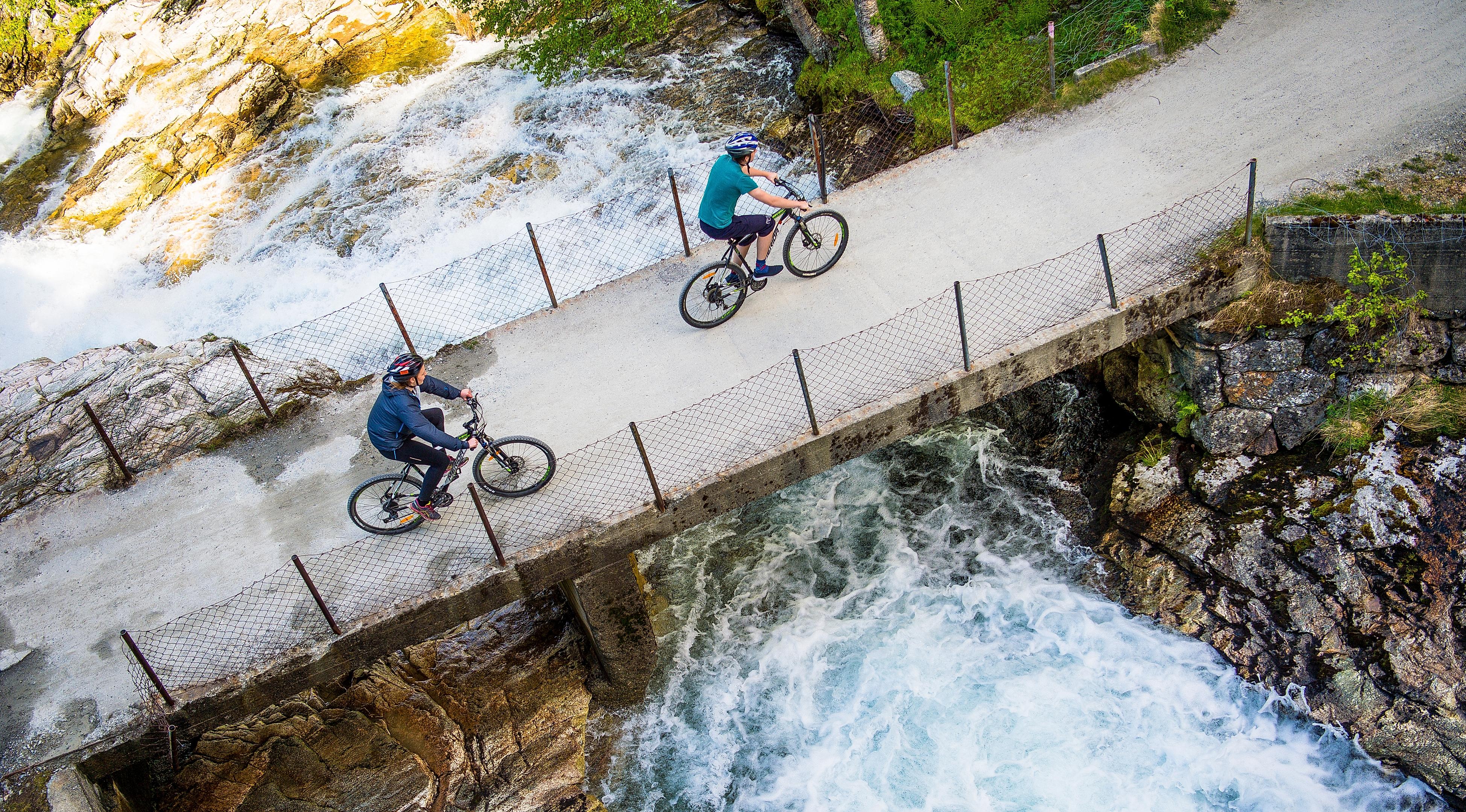 Two cyclists crossing a bridge on the river on the Rallarvegen, Fjord Norway
