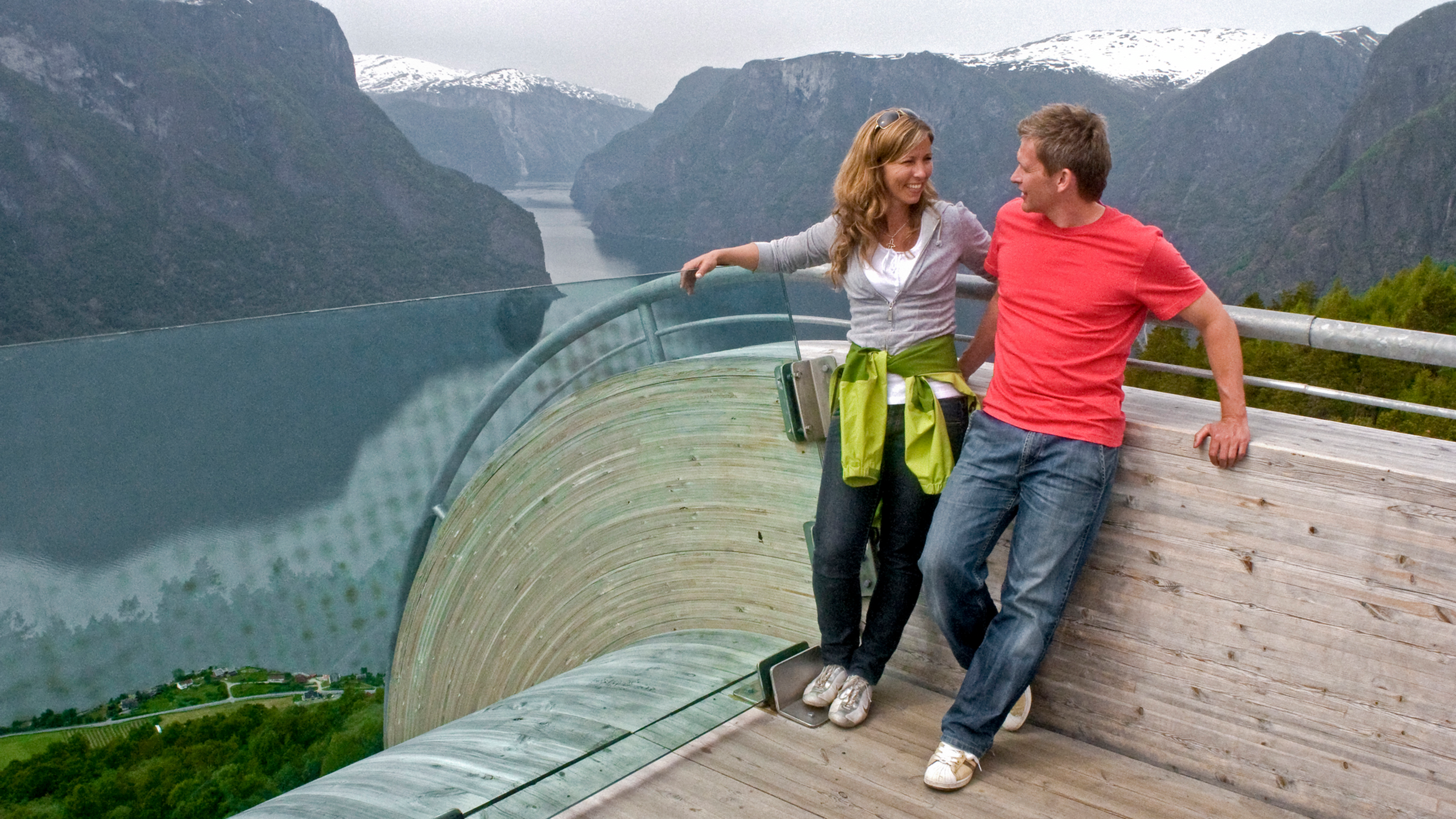 Two people holding each other at a viewpoint overlooking the fjord and mountains