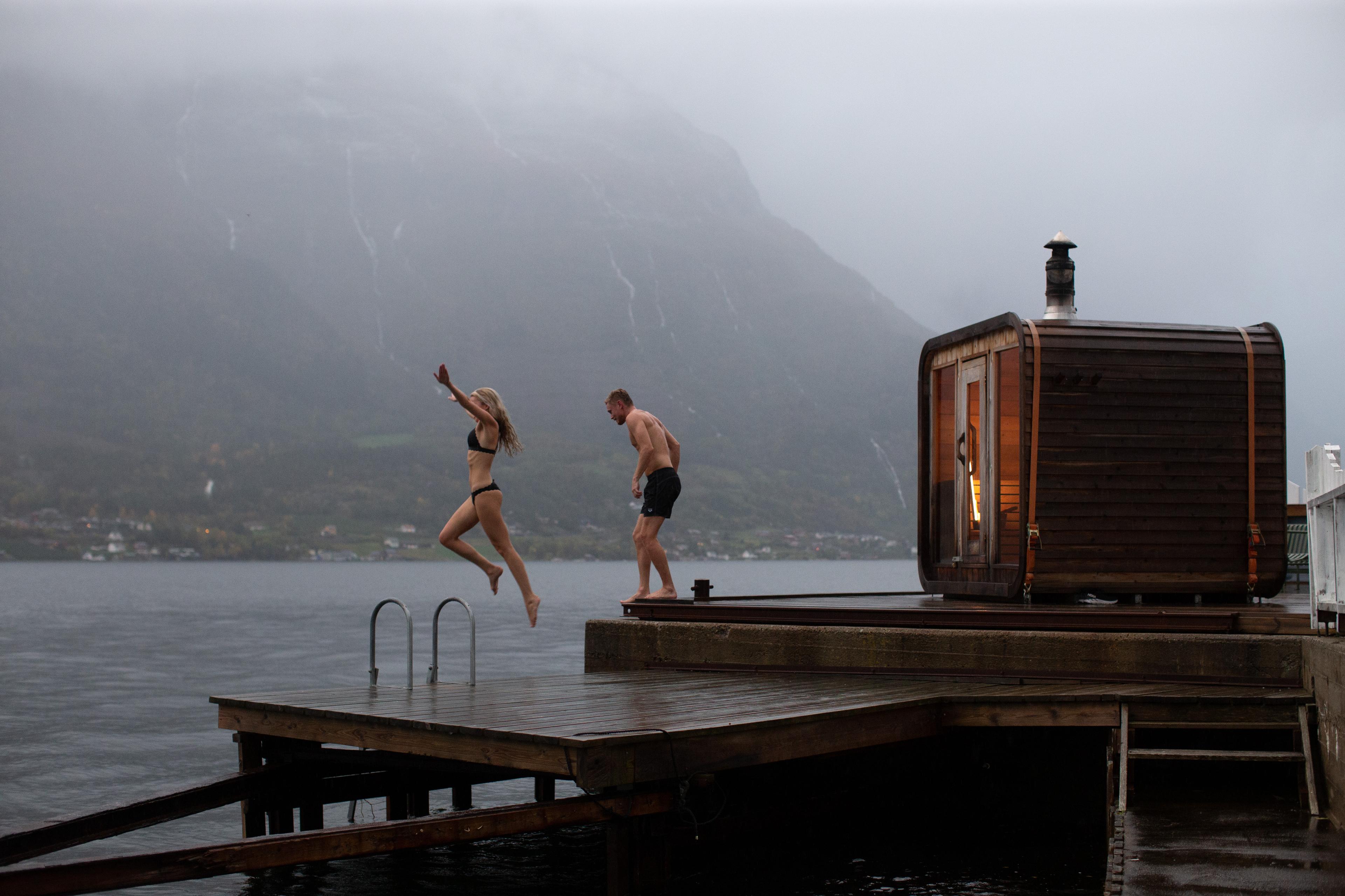 A couple jumping from a sauna into the water.