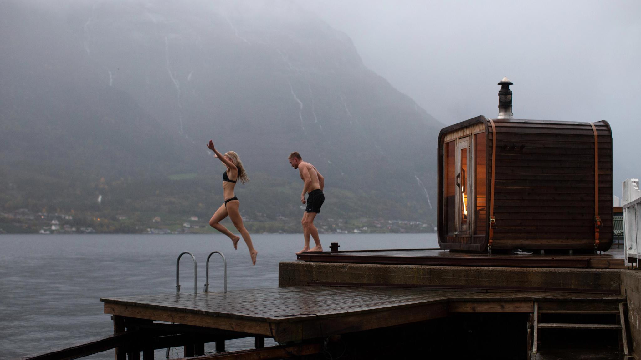 A couple jumping from a sauna into the water.