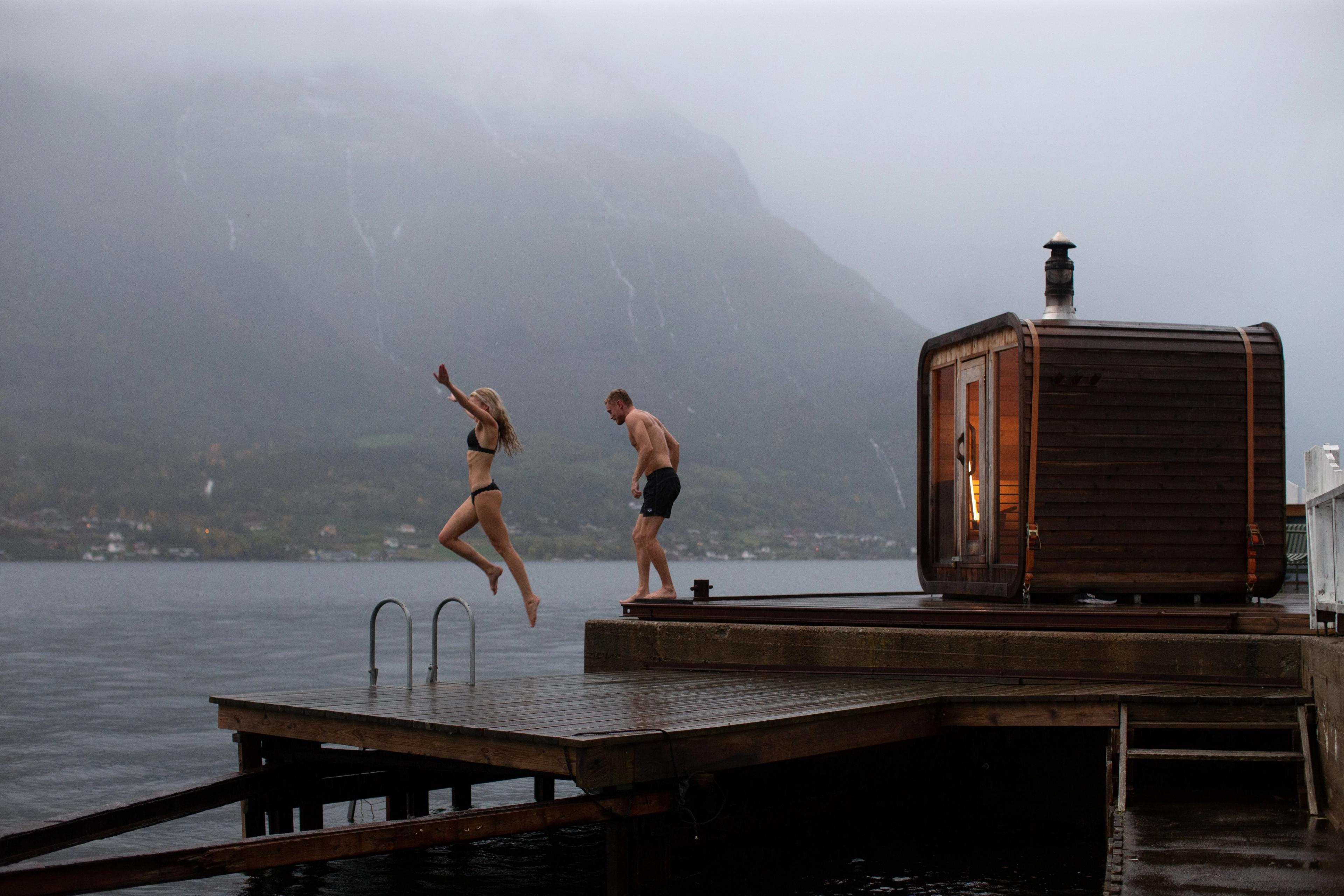 A couple jumping from a sauna into the water.