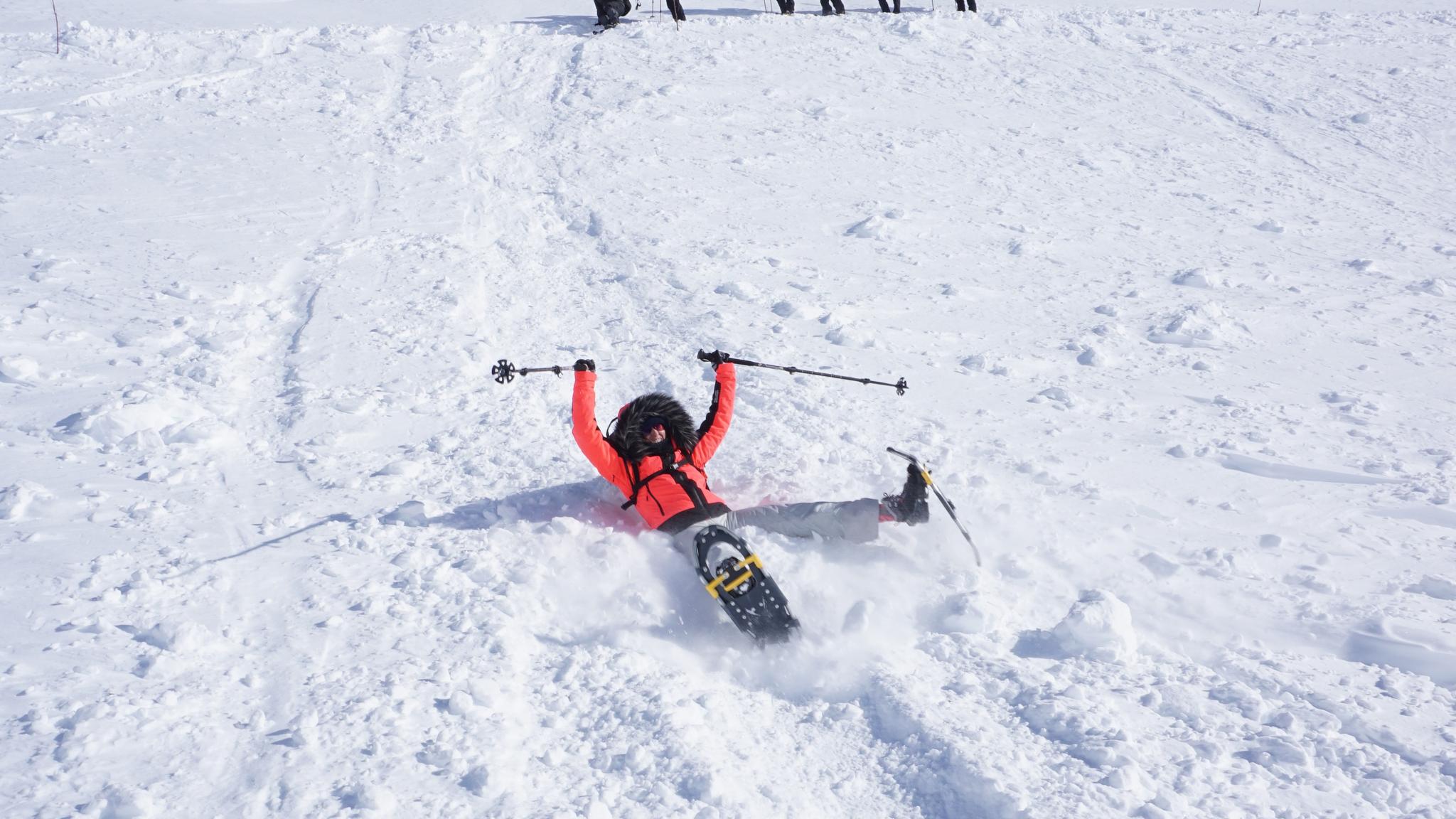 A group is snowshoeing to Trolltunga in Fjord Norway in winter, and one woman is sliding down the hill on her butt, smiling.