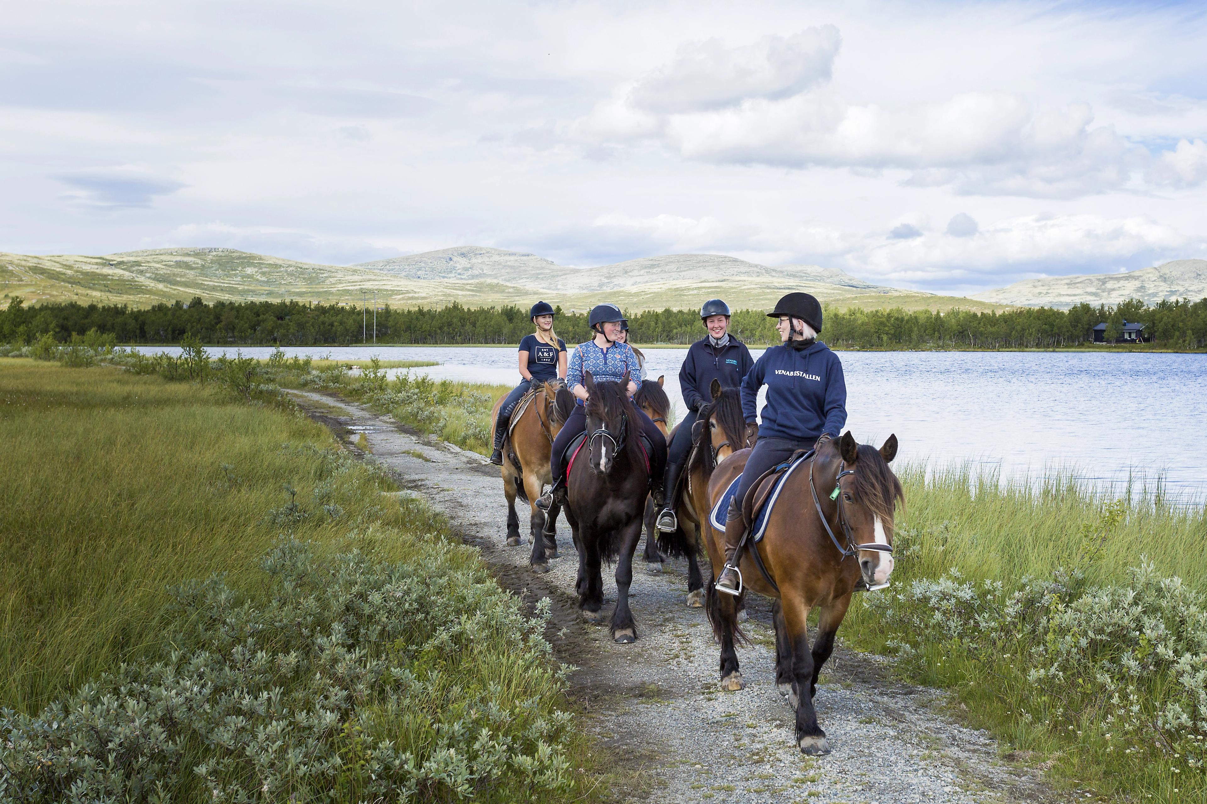Four women riding horses by a lake