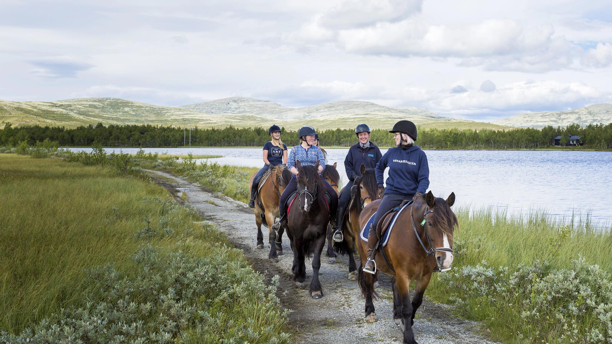 Four women riding horses by a lake