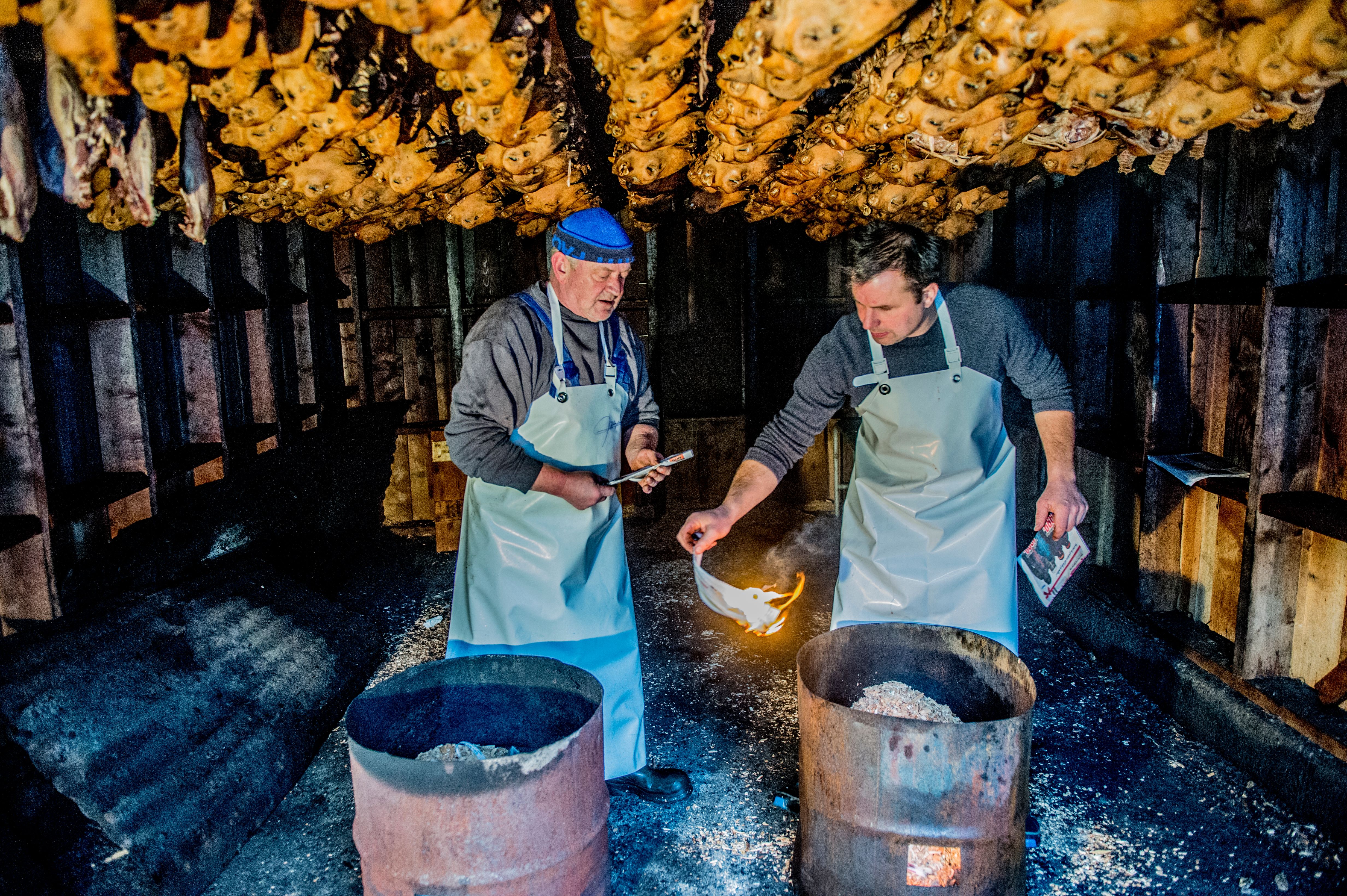 Two men under rows of smalahove sheep heads at Smalahovetunet in Voss, Fjord Norway