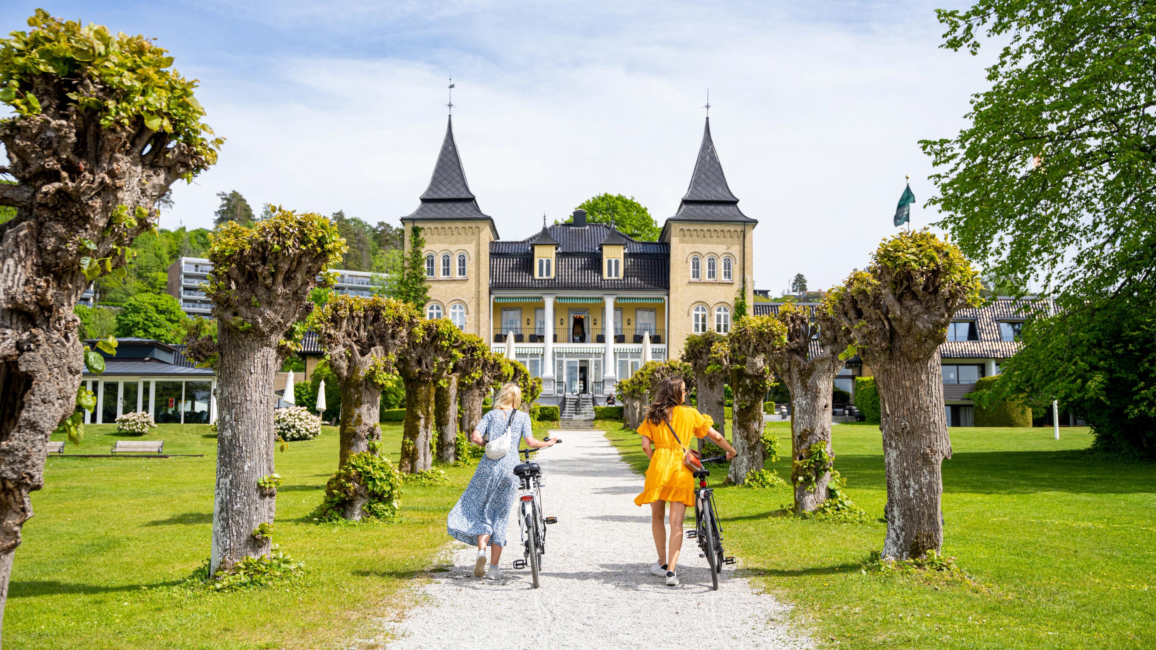 Two women walking besides their bikes on the way to a manor hotel.