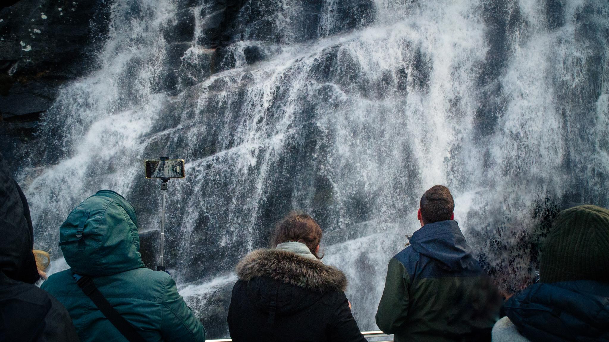 Passengers on a cruise boat getting a refreshing spray from the waterfall.