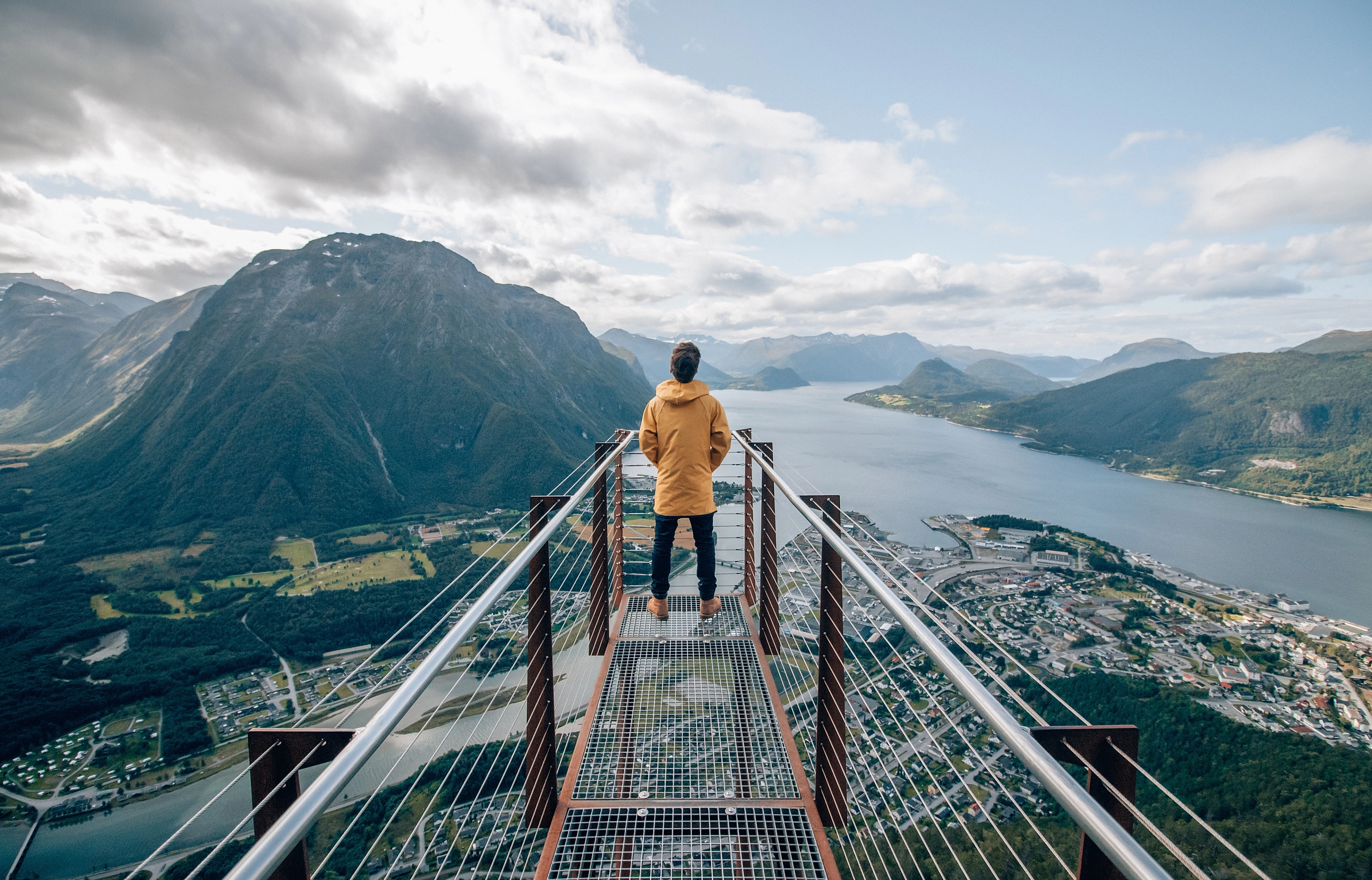 A person standing at the tip of Rampestreken viewpoint, looking out at the fjord and mountains of Åndalsnes in Northwest, Fjord Norway.