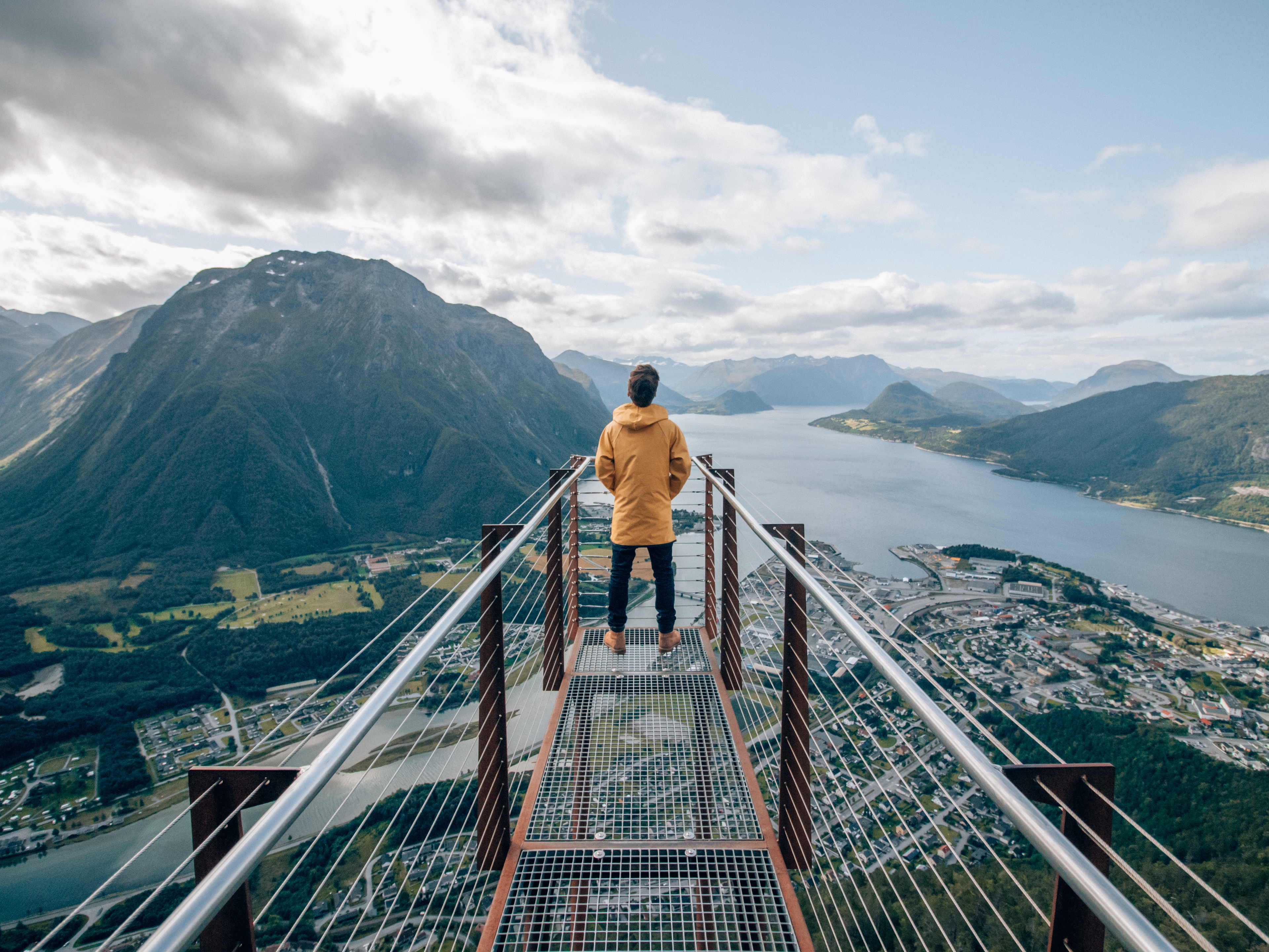 A person standing at the tip of Rampestreken viewpoint, looking out at the fjord and mountains of Åndalsnes in Northwest, Fjord Norway.
