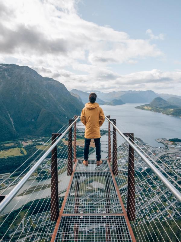 Een persoon die aan het uiteinde van het uitkijkpunt Rampestreken staat en uitkijkt over het fjord en de bergen van Åndalsnes in Noordwest, Fjord-Noorwegen