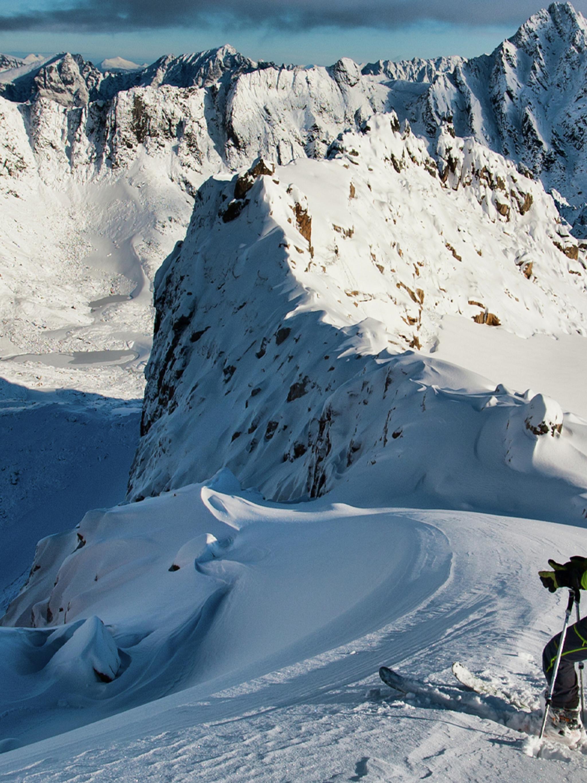 En mann på topptur på ski står klar til å kjøre nedover fjellet