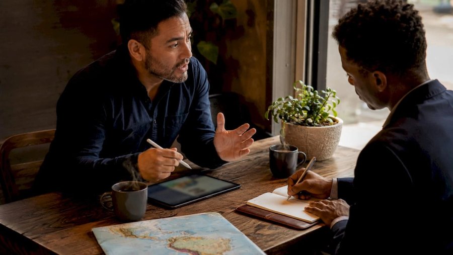 Two men discussing recruitment strategies over café table