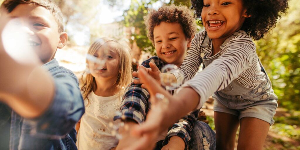 Lachende Kinder spielen draußen und strecken ihre Hände in die Kamera.