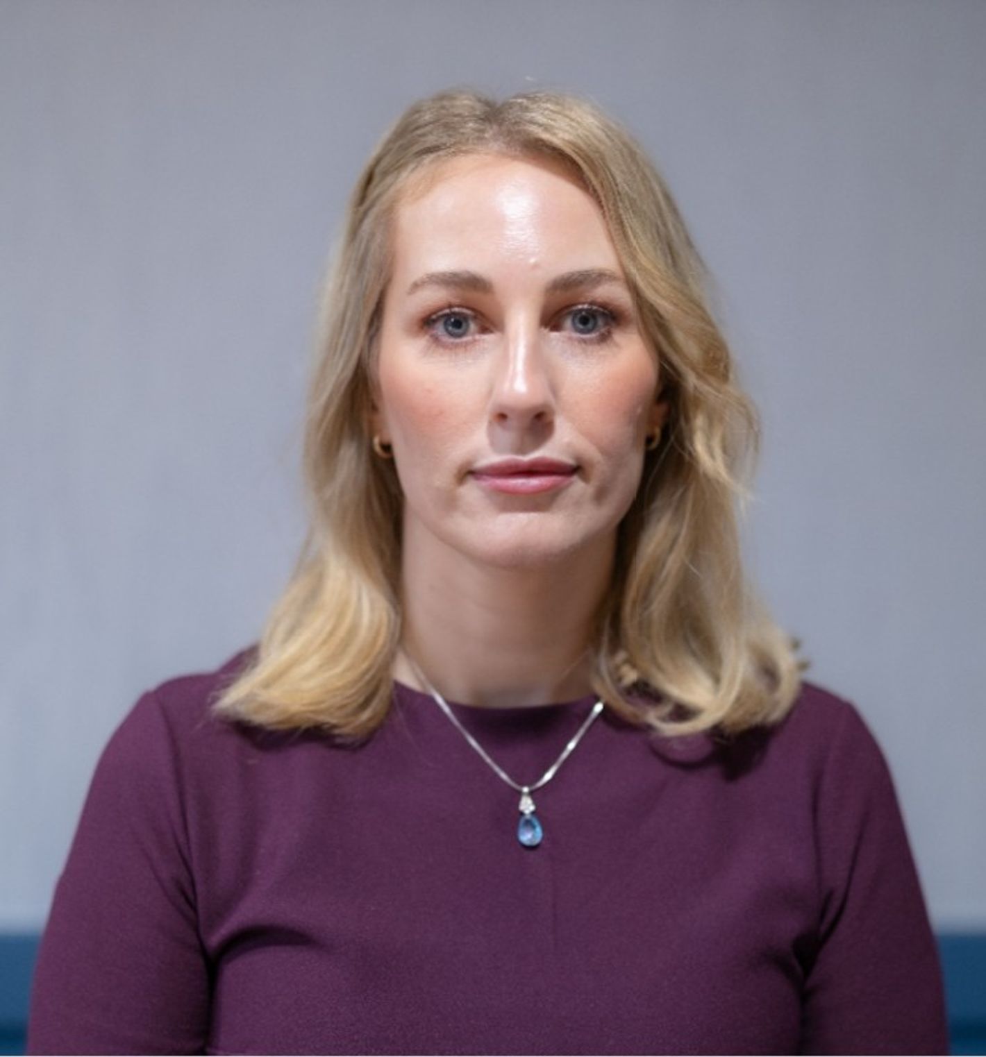 Hege Thuen-Overvåg - Blonde woman in a purple top with a blue pendant necklace, looking straight at the camera against a plain background