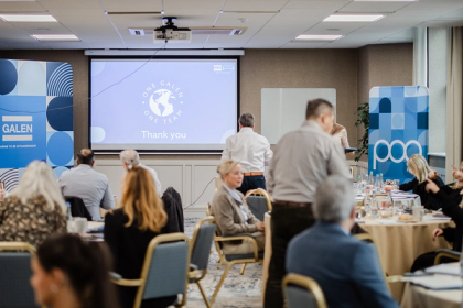 Attendees seated at round tables during a Galen business meeting, with a Thank You slide projected on screen