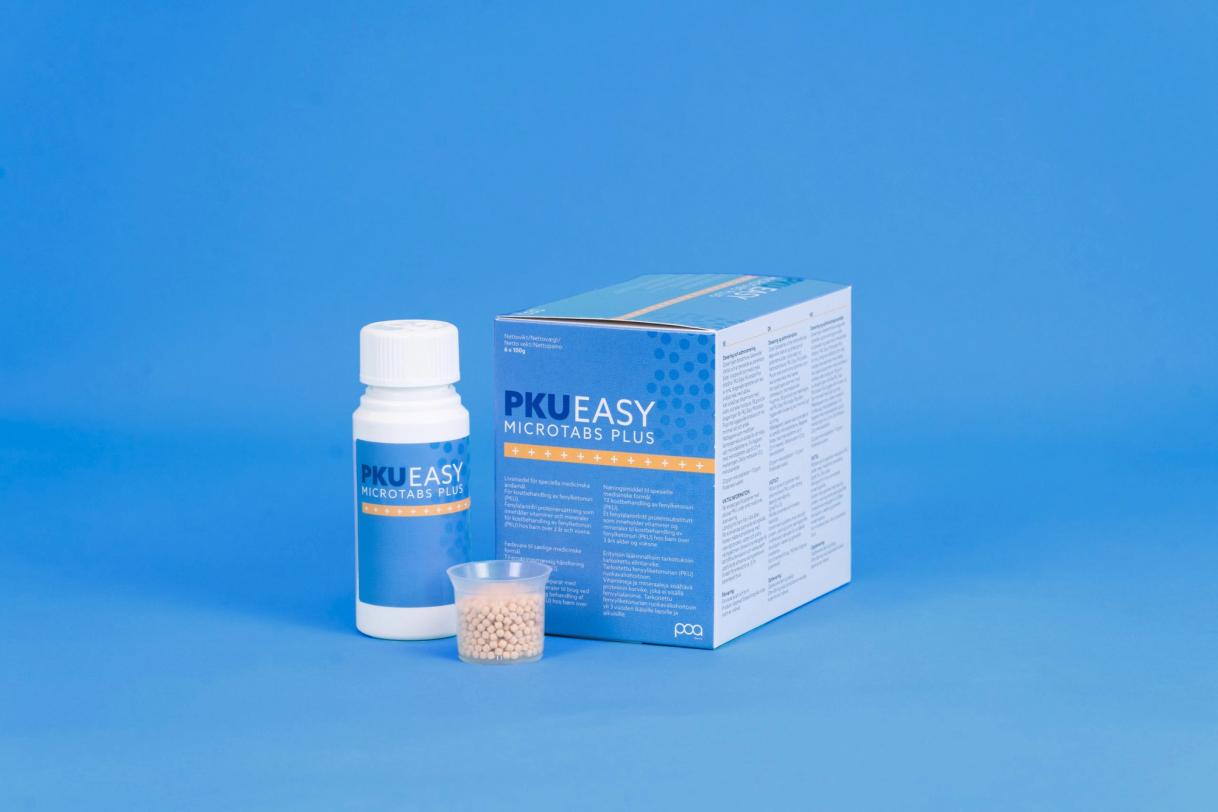 PKU Easy Microtabs Plus bottle, box, and small cup of microtablets displayed on a blue background