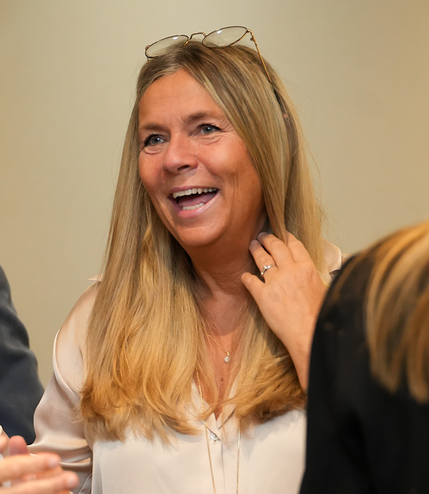 Annika Kindahl - smiling blonde woman, light top, hand raised near face