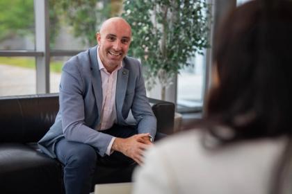 Smiling man in a blazer seated on a leather sofa having a conversation in a bright modern office