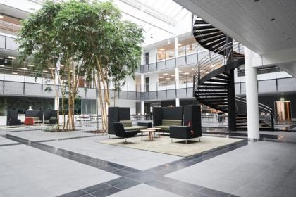 Modern corporate atrium with tall bamboo trees, lounge seating, spiral staircase, and open upper-floor walkways